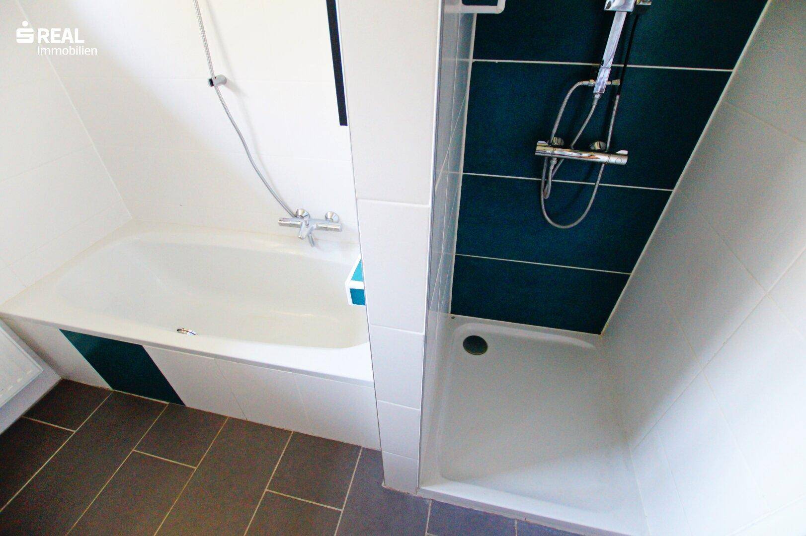 Badezimmer mit Badewanne und Duschbereich, ausgestattet mit modernen Fliesen und blauen Akzenten.