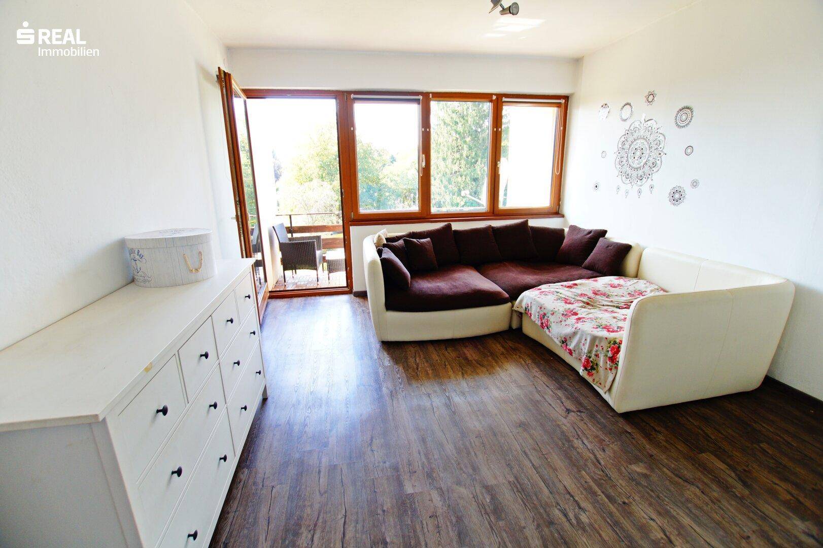 Helles Wohnzimmer mit großem Ecksofa, weißer Kommode und direktem Zugang zum Balkon.