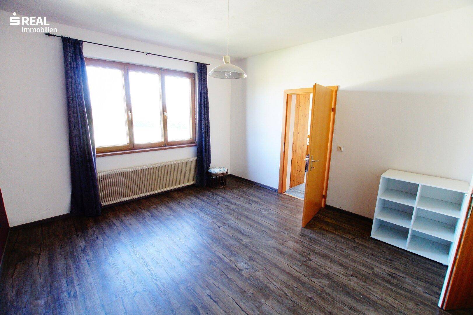 Heller Raum mit Laminatboden, Heizkörper und Fenster mit dunkelblauen Vorhängen.