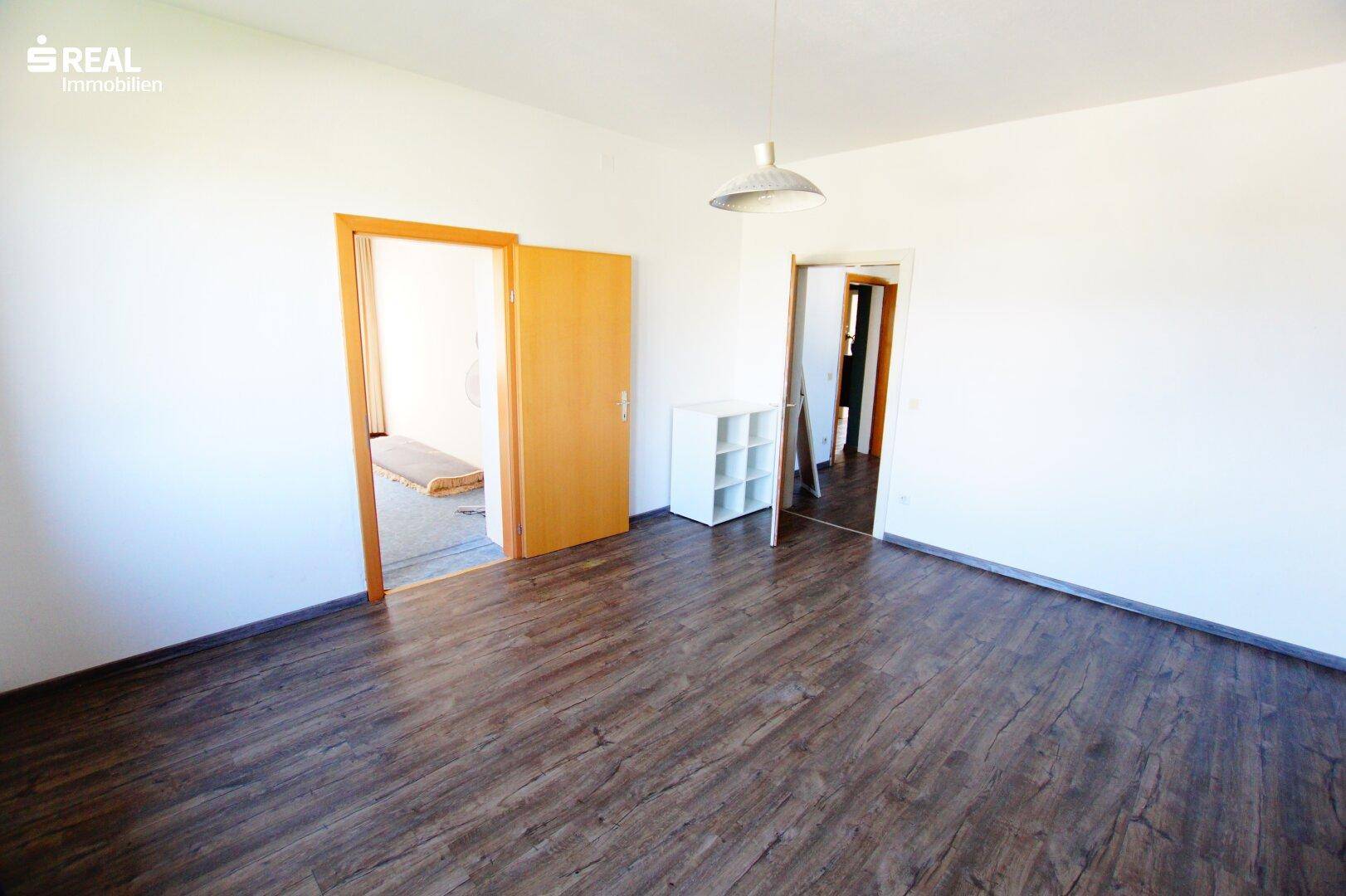 Geräumiges Schlafzimmer mit Laminatboden und Zugang zu einem angrenzenden Bereich mit Bett.