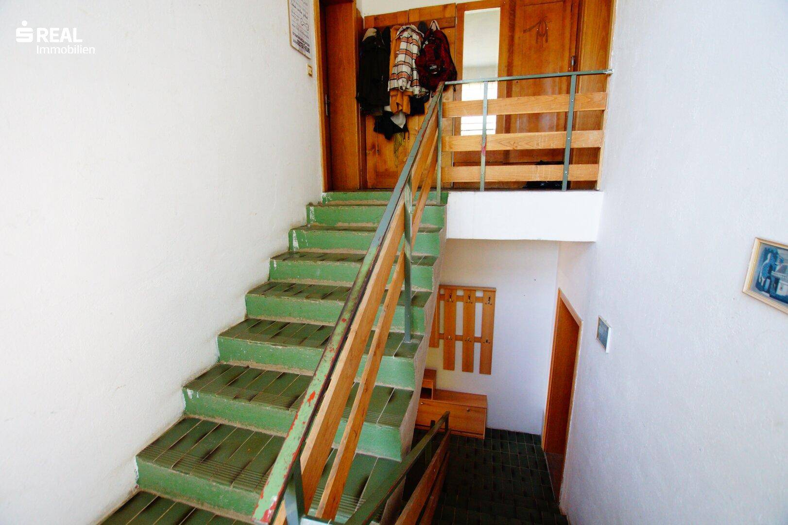 Innenliegende Treppe mit grünen Fliesenstufen und Holzgeländer, verbindet die Stockwerke.