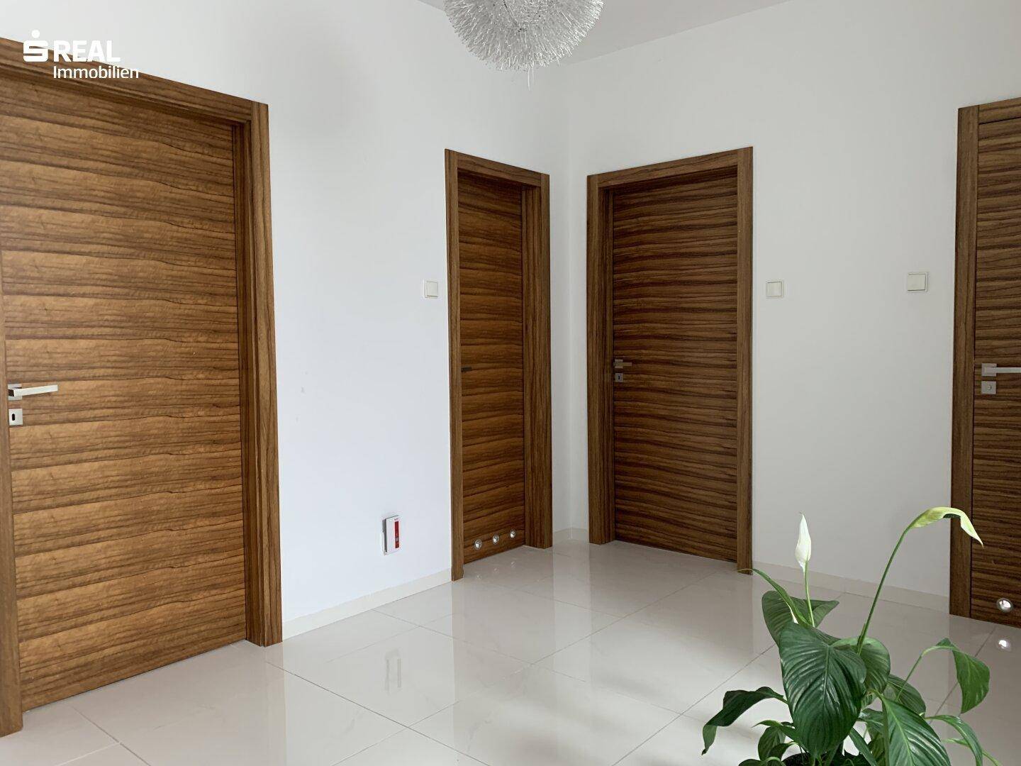 Heller Flur mit mehreren Holztüren, weißen Wänden und glänzendem Fliesenboden.