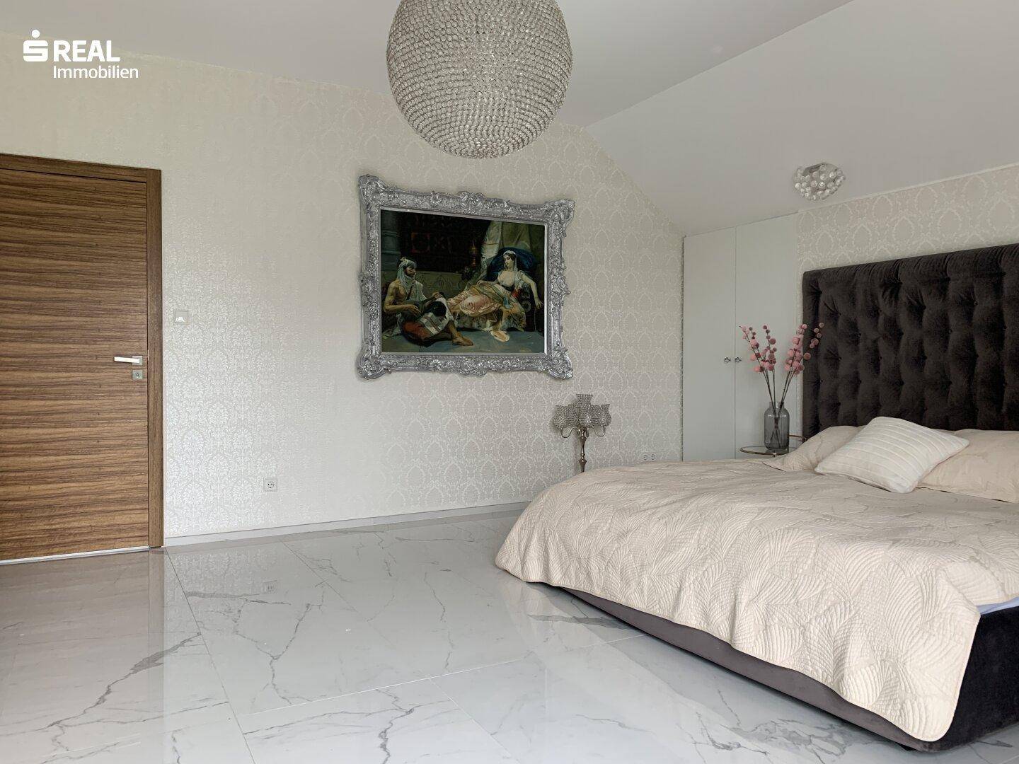 Elegantes Schlafzimmer mit großem Bett, gemusterter Tapete und Holztür.