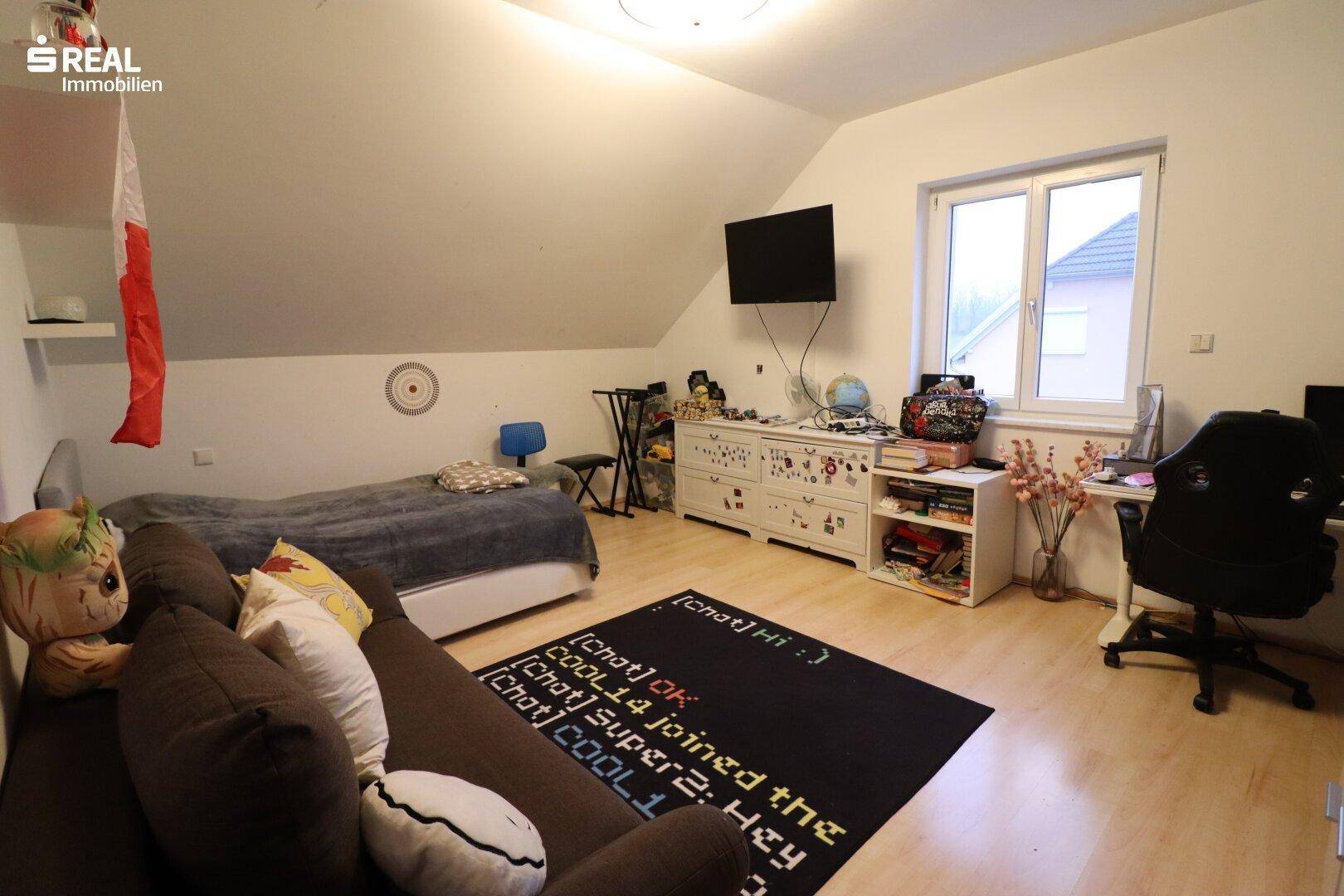 Helles Kinder- oder Gästezimmer mit Holzboden, Schreibtisch und Dachschräge.