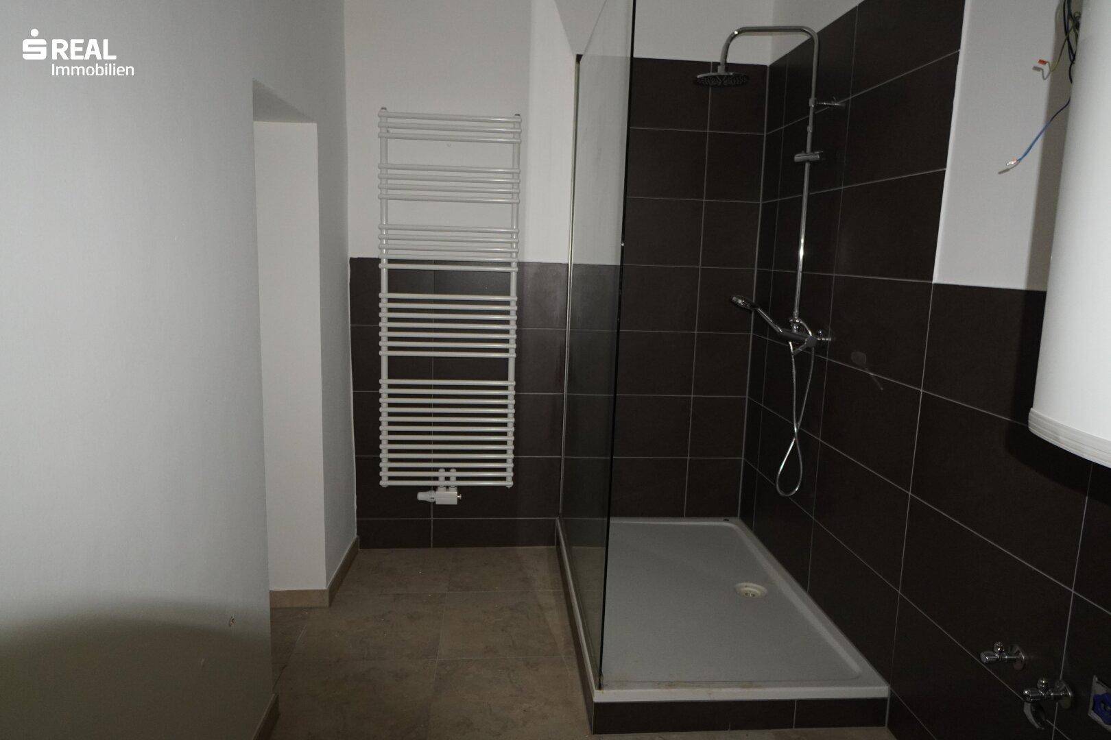 Modernes Badezimmer mit großer Duschkabine, dunklen Fliesen und beheiztem Handtuchhalter.