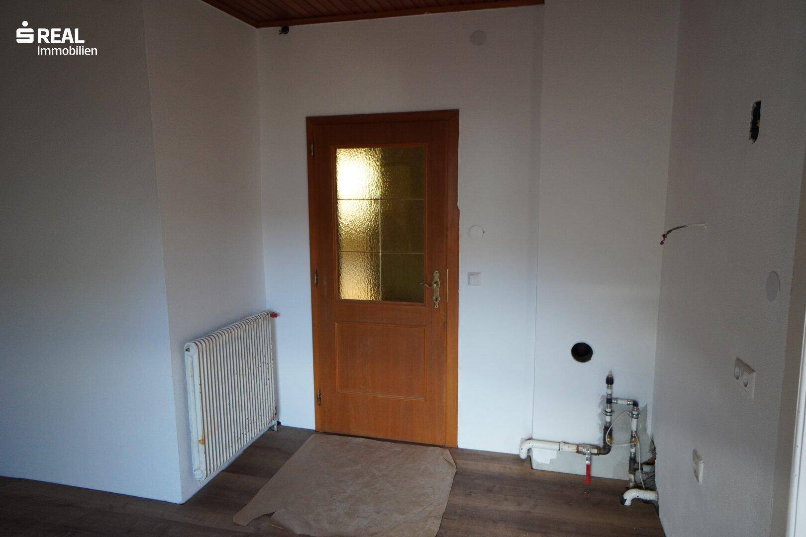 Unmöblierter Küchenbereich mit Heizkörper und Holztür, bereit für die Installation einer Küche.