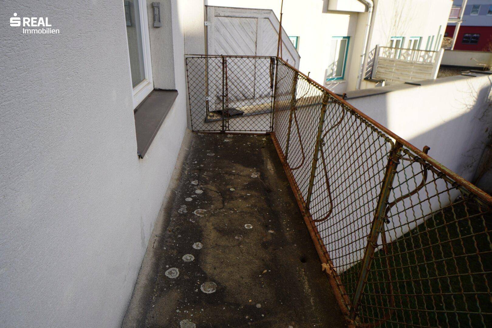 Kleiner, sanierungsbedürftiger Balkon mit Metallgeländer und Blick auf die Umgebung.