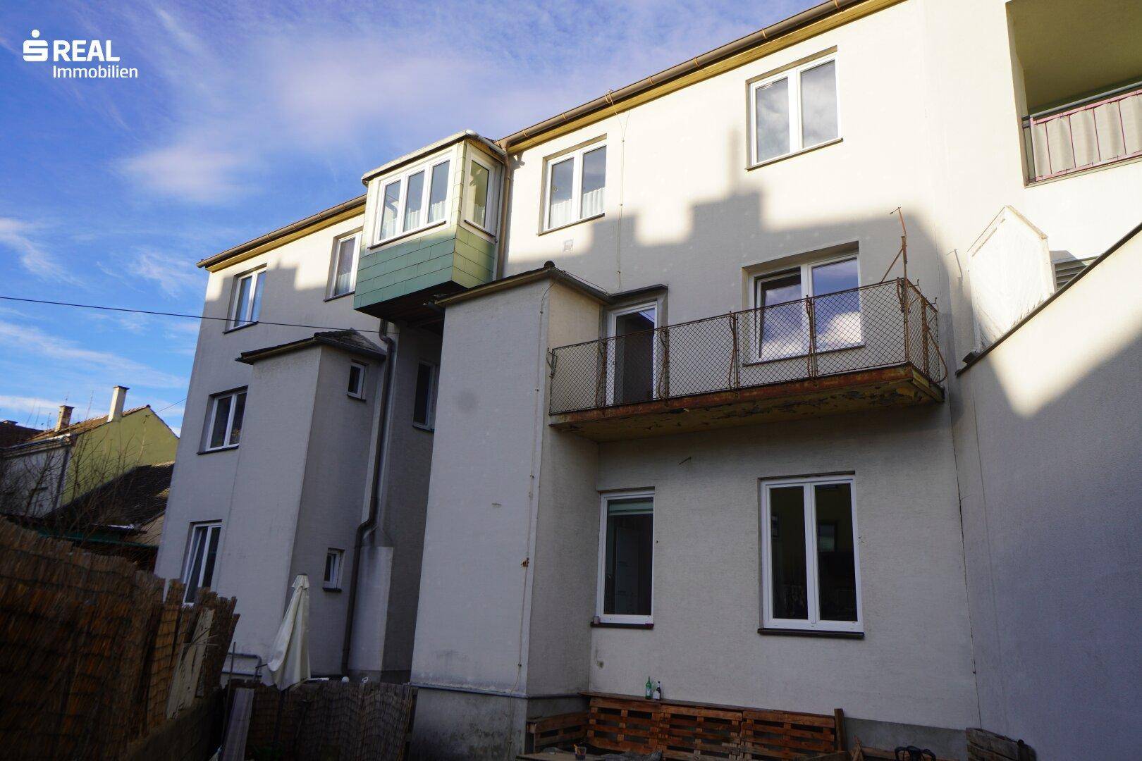 Rückansicht eines Mehrfamilienhauses mit Balkonen und verschiedenen Fensterformen.