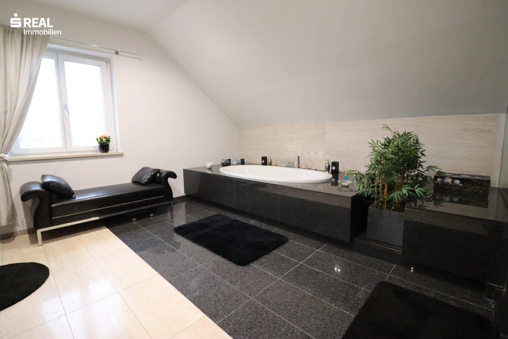 Geräumiges Badezimmer mit großer Badewanne, dunklem Fliesenboden und Dachschräge.