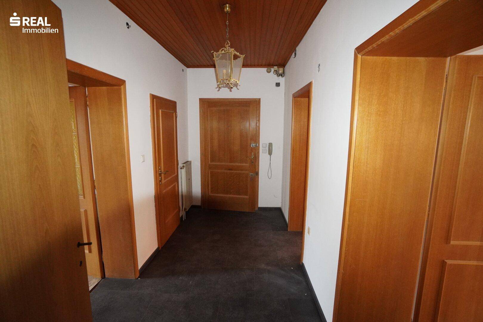 Eingangsbereich mit dunklem Teppichboden, Holzdecke und mehreren Holztüren zu den Zimmern.