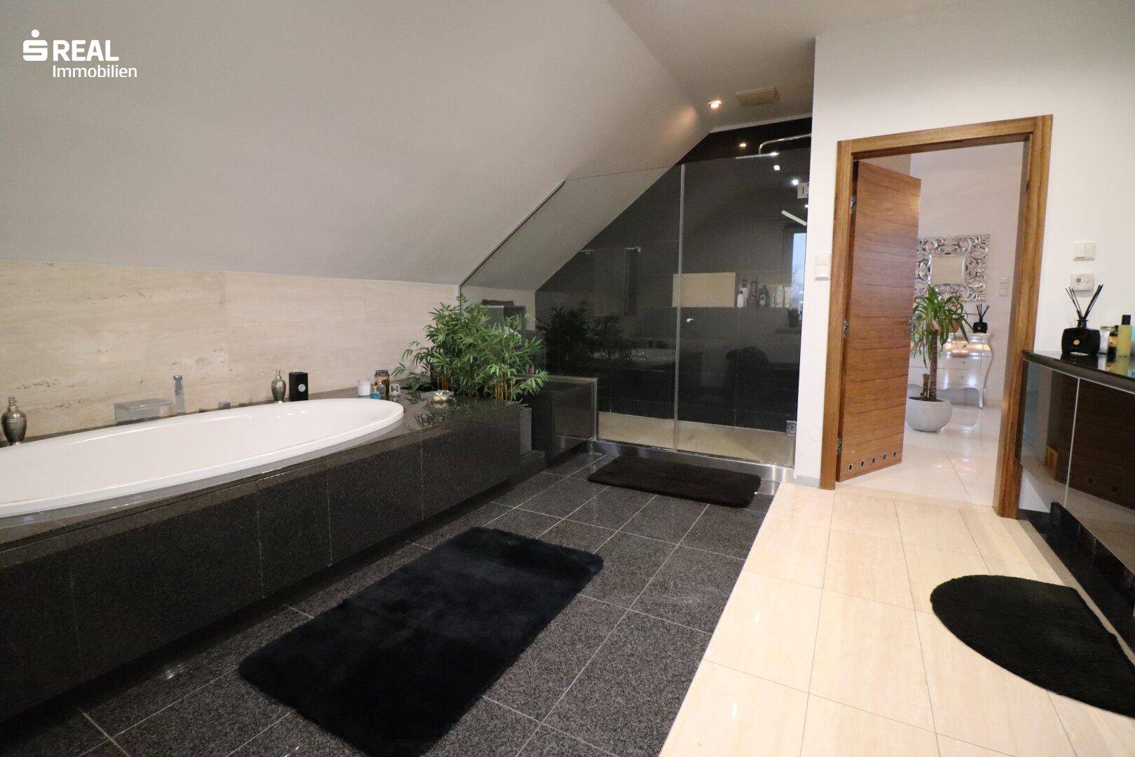 Elegantes Badezimmer mit großer Badewanne, begehbarer Dusche und dunklem Fliesenboden.
