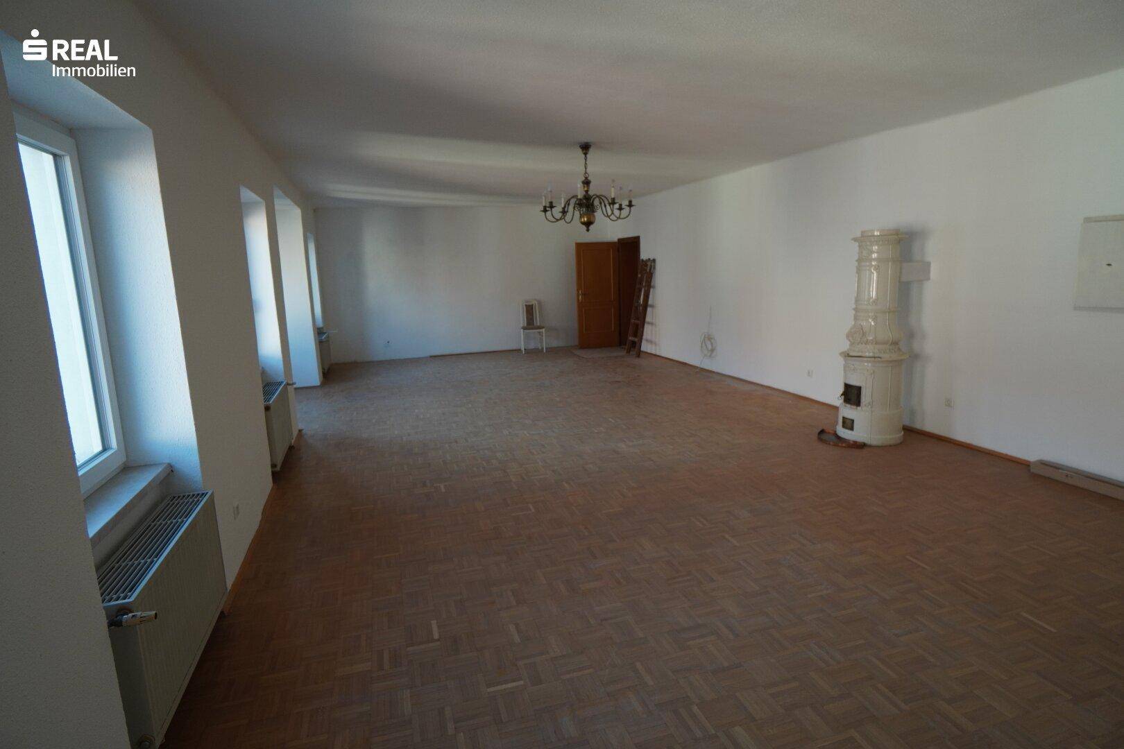 Helles Wohnzimmer mit traditionellem Kachelofen und Parkettboden, bereit zur individuellen Gestaltung.