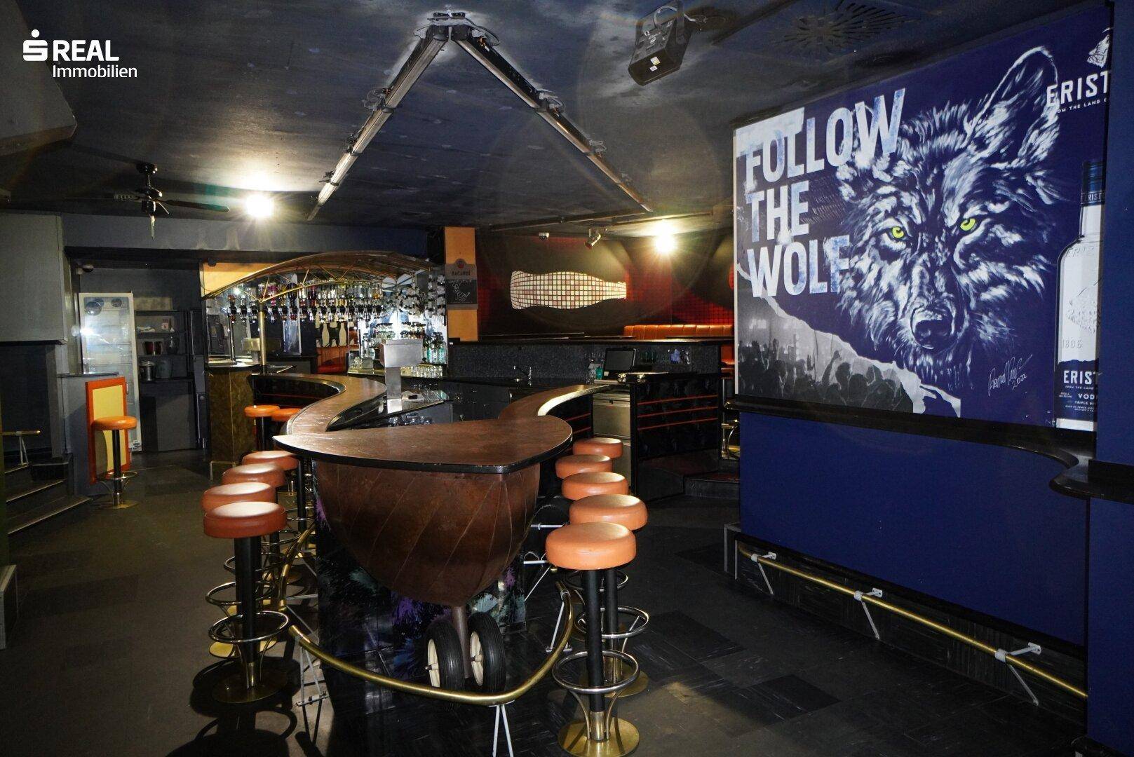 L-förmige Bar mit Hockern und großer Wandgrafik eines Wolfes in dunkler Atmosphäre.