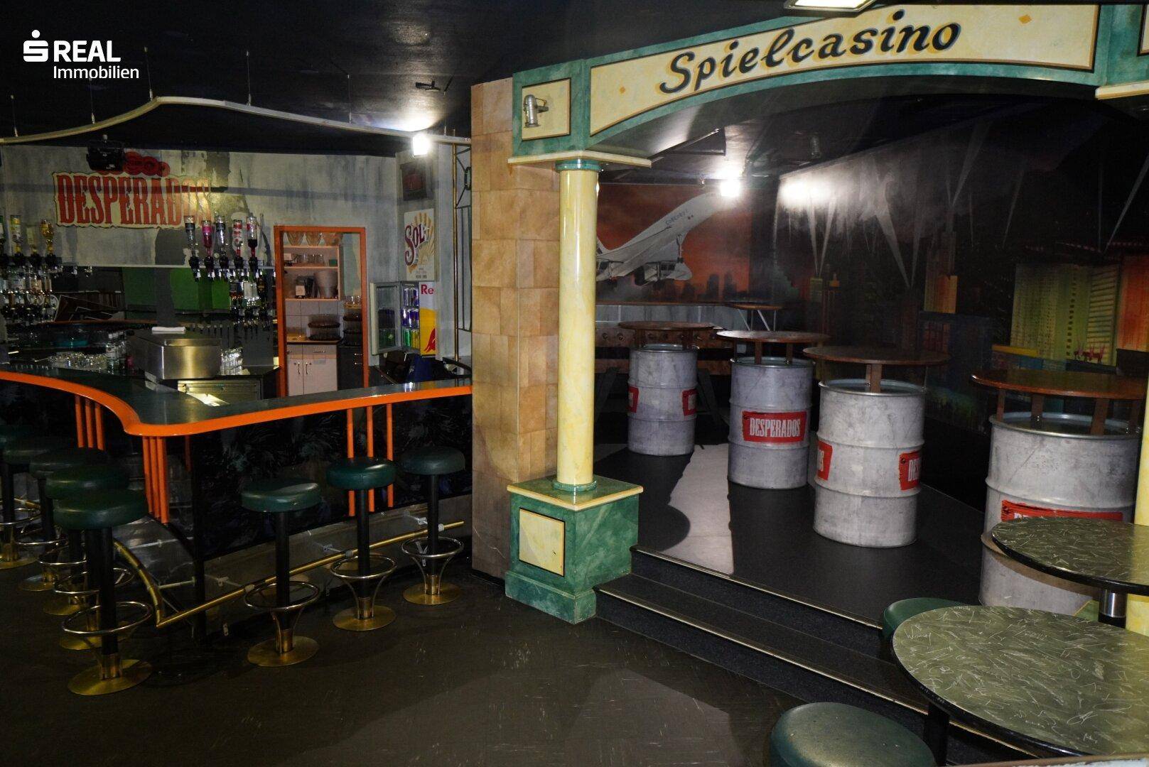 Barbereich mit Säulen, Stehtischen und einem Schild, das auf ein Spielcasino hinweist.
