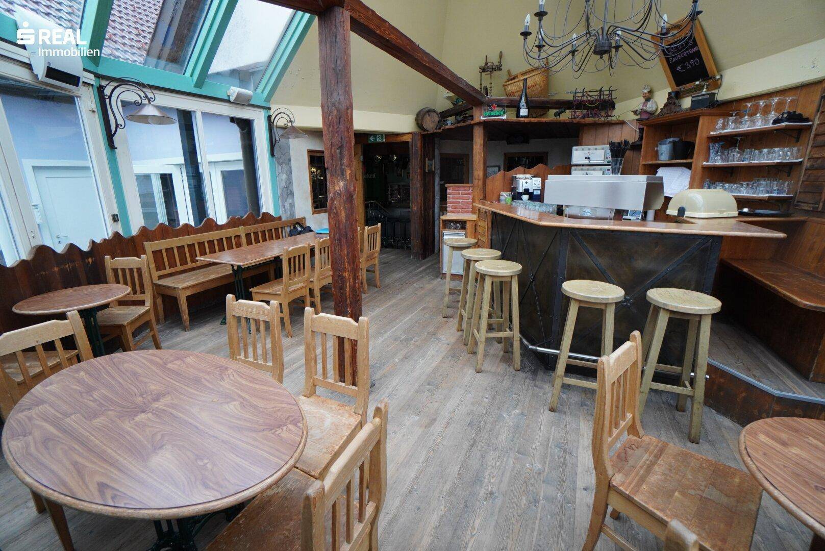Heller Wintergarten mit Holztischen, Bänken und einer kleinen Bar.