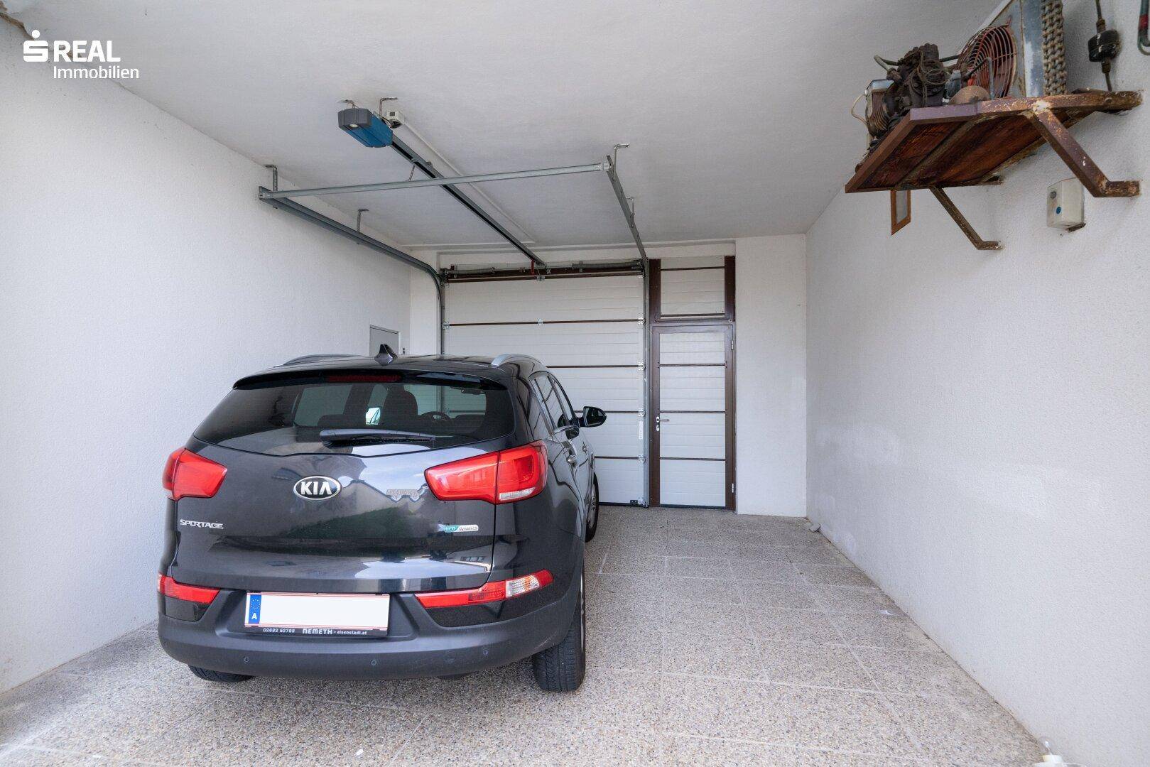 Innenansicht einer Garage mit einem geparkten Auto und einem automatischen Garagentor.
