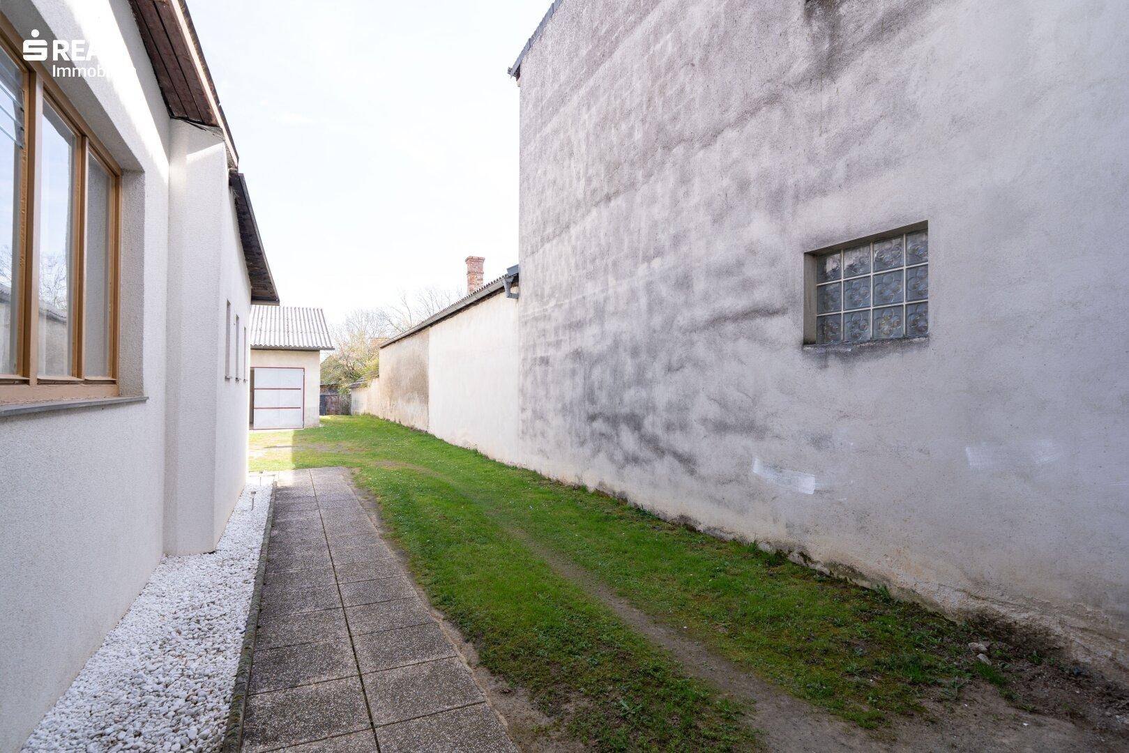 Schmaler Weg zwischen zwei Gebäuden mit einer grauen Wand und einem kleinen Fenster.