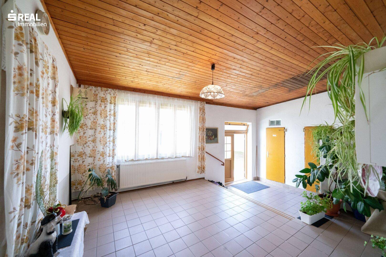 Geräumiger Eingangsbereich mit Holzdecke, Fliesenboden und großen Fenstern, die viel Tageslicht hereinlassen.