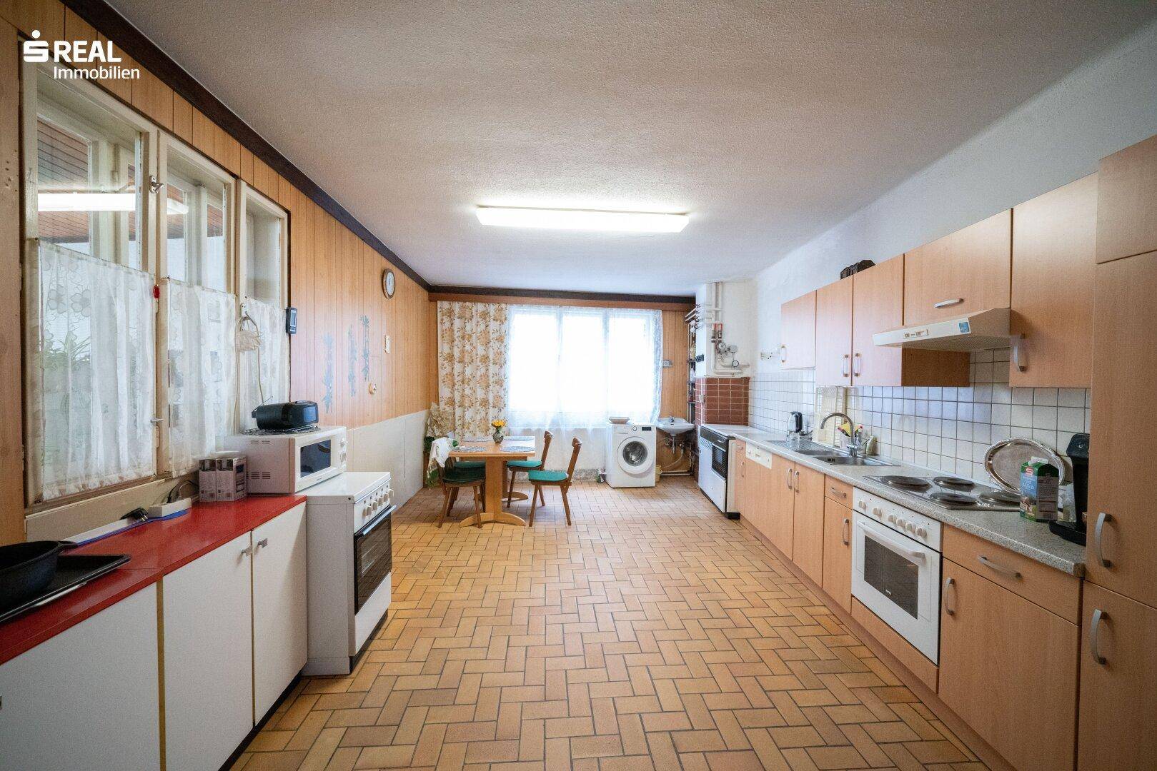 Geräumige Wohnküche mit Holzschränken, Fliesenboden und Essbereich am Fenster.
