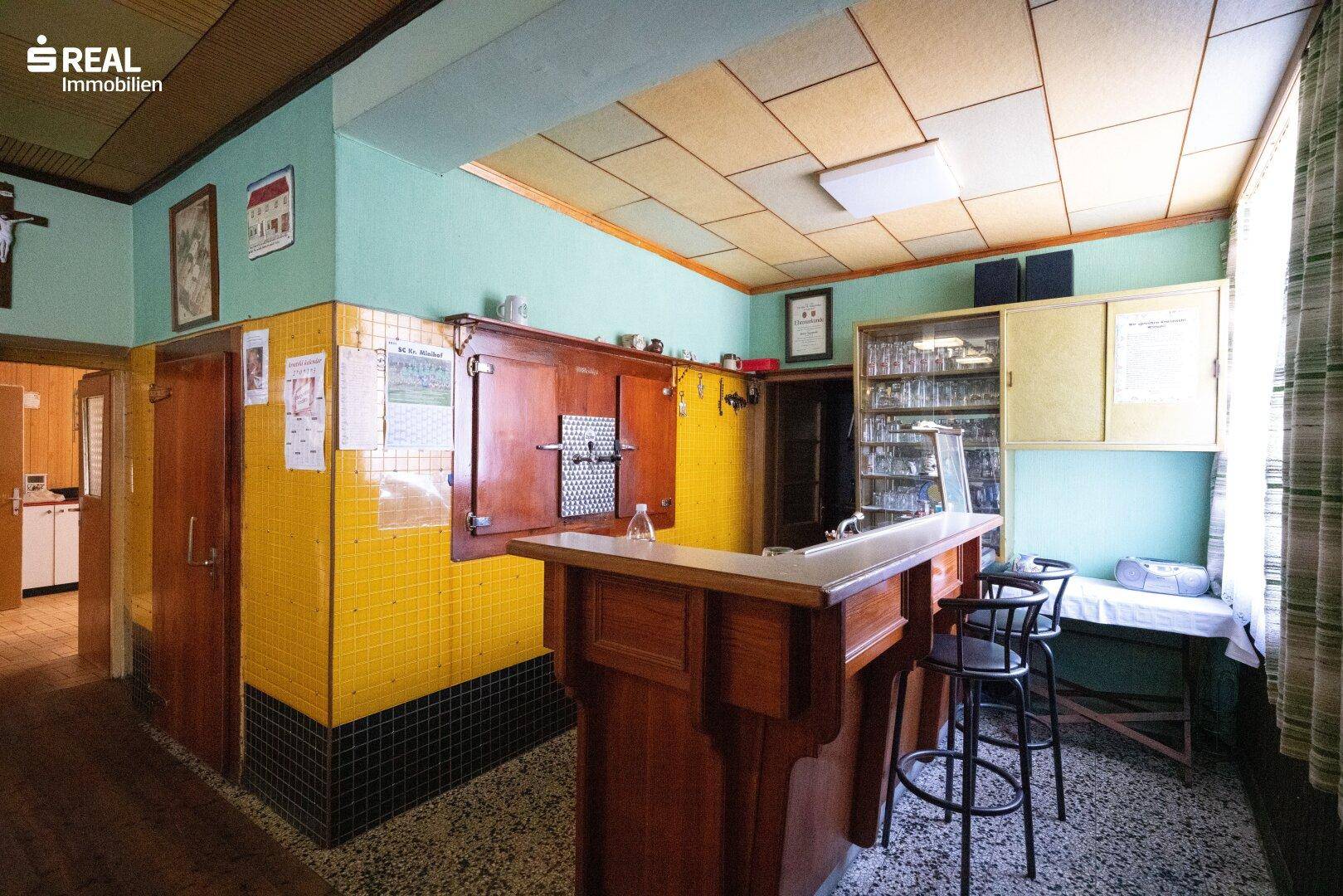 Gemütlicher Barbereich mit Holztresen, Hockern und gelben Fliesen an der Wand.
