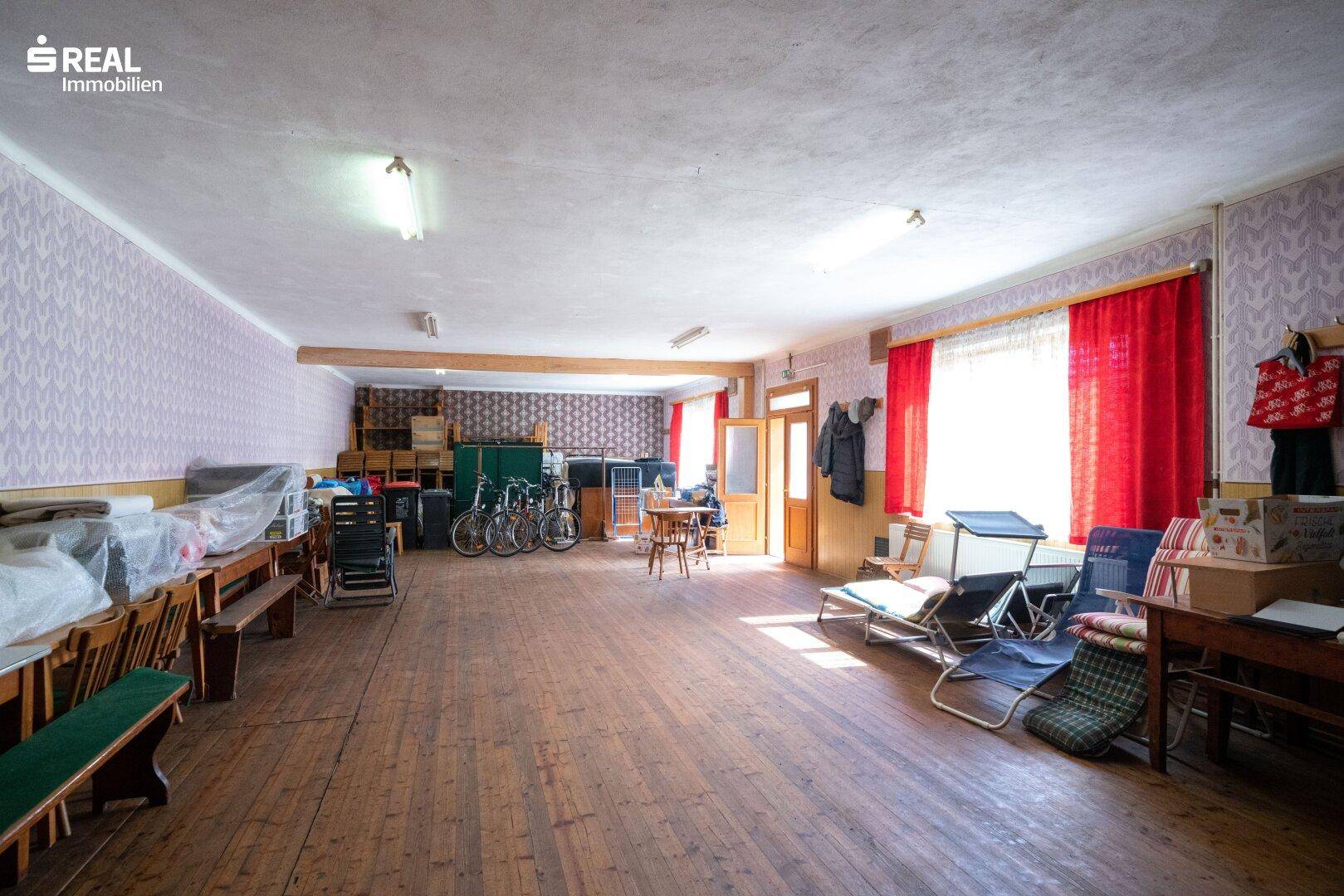 Großer Raum mit Holzboden, roten Vorhängen und verschiedenen Möbeln und Gegenständen.