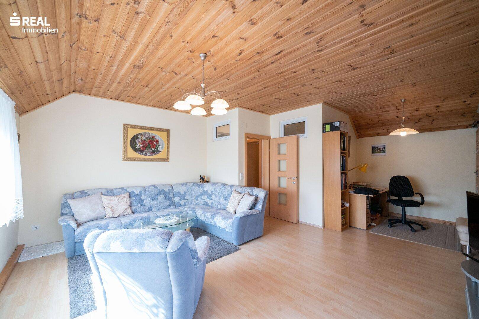 Gemütliches Wohnzimmer mit Ecksofa, Holzdeckenverkleidung und integriertem Arbeitsbereich.