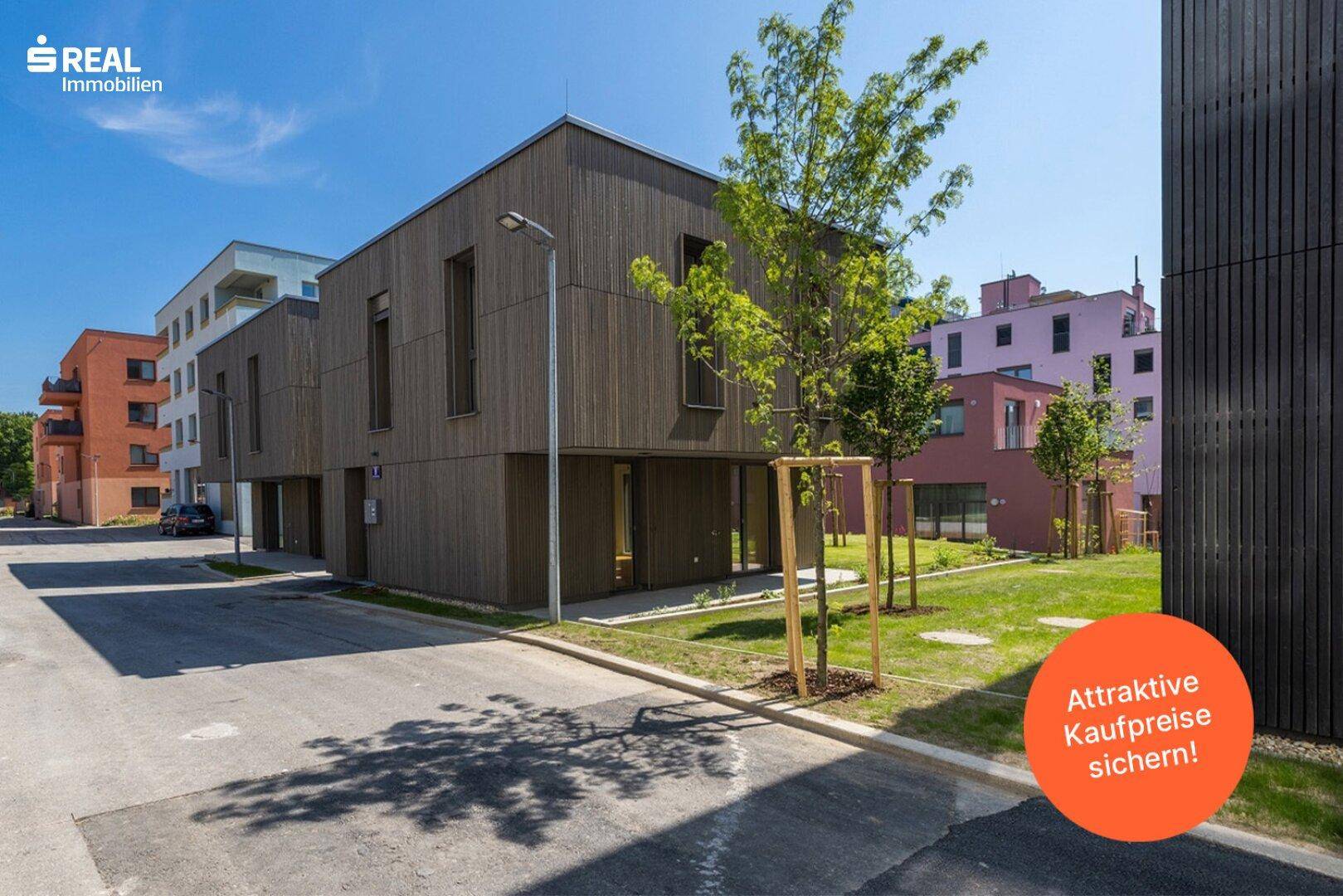 Moderne Wohngebäude mit dunkler Holzfassade entlang einer Straße in einer neu entwickelten Wohngegend.