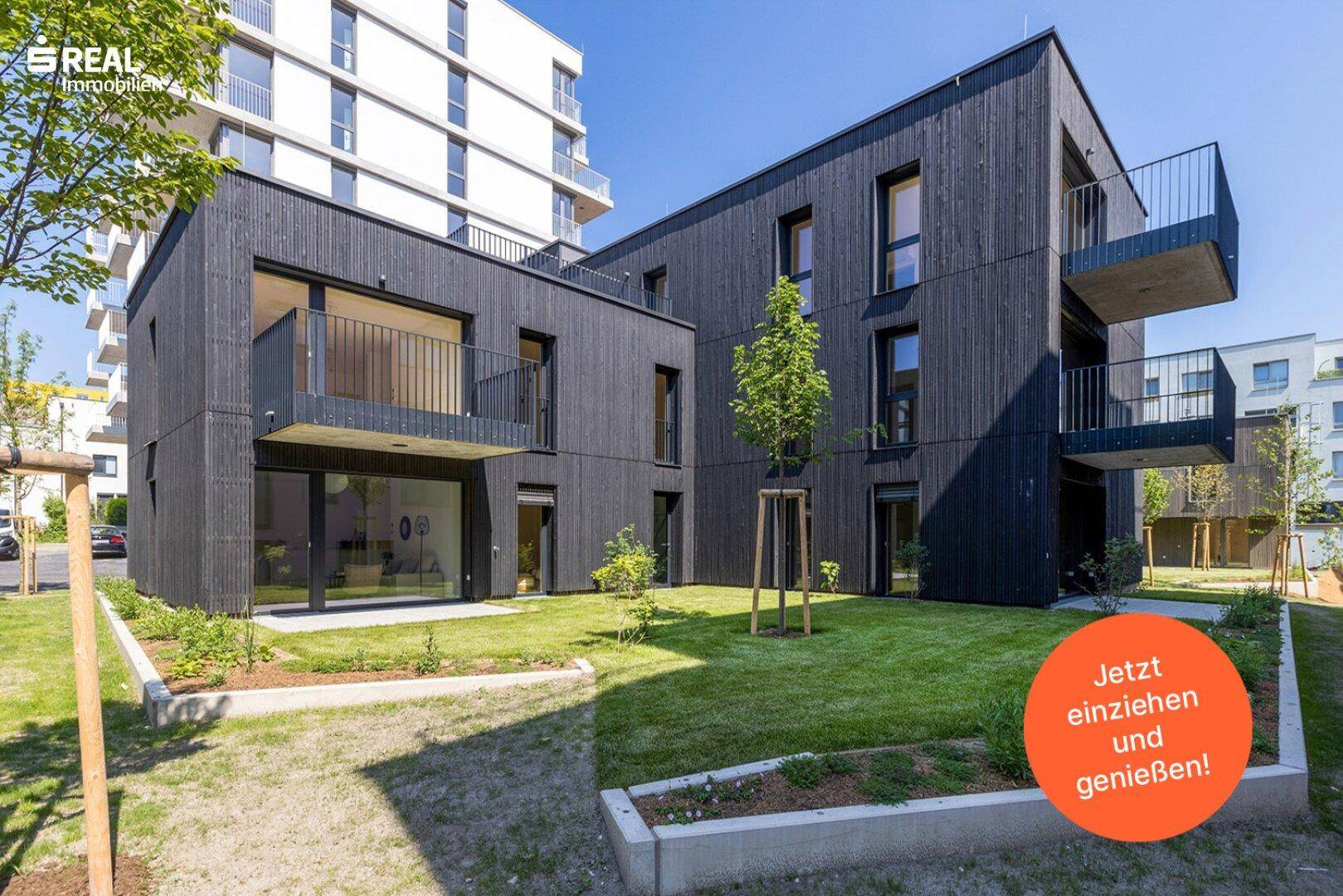 Attraktive Neubauwohnungen mit dunkler Holzfassade, Balkonen und Zugang zu einer grünen Rasenfläche.