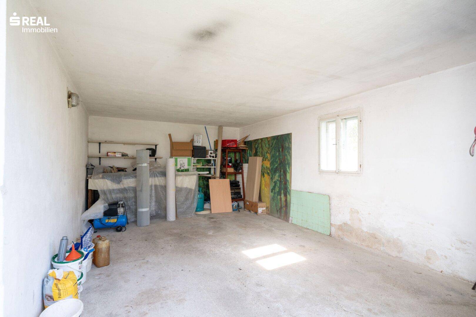 Geräumige Garage mit Betonboden und Fenster, genutzt als Abstellraum.