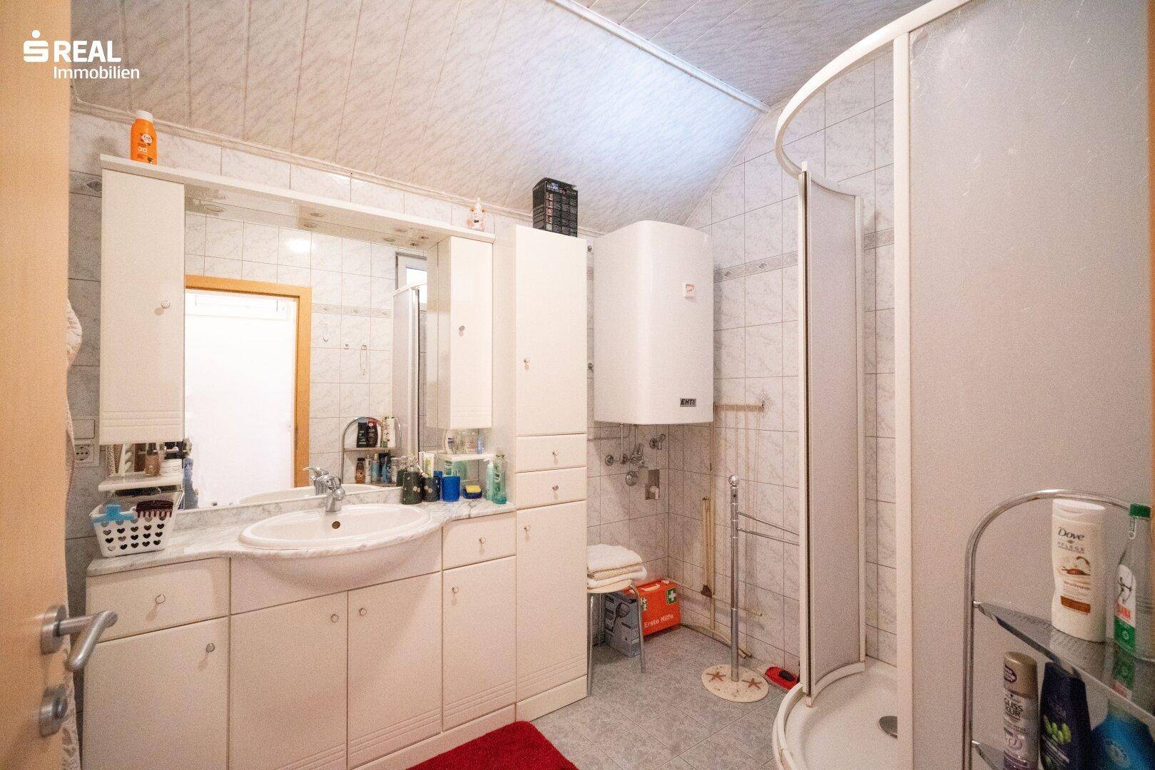 Badezimmer mit Duschkabine, Waschbecken und weißen Fliesen an Wänden und Boden.