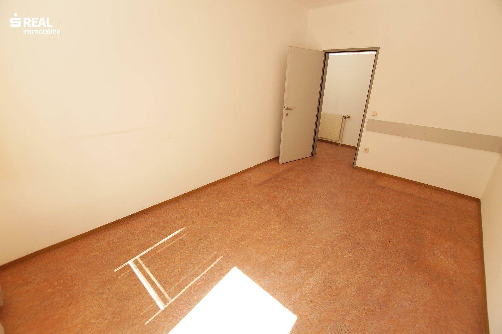 Leerer Büroraum mit braunem Bodenbelag und weiß gestrichenen Wänden.