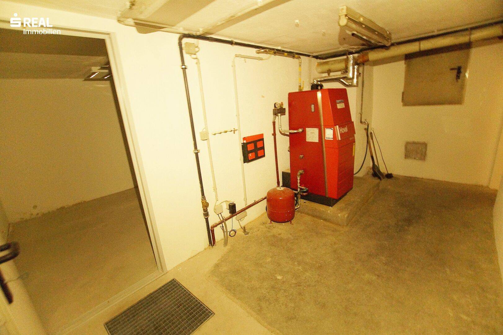 Kellerraum mit roter Heizungsanlage, sichtbaren Rohren und Betonboden.