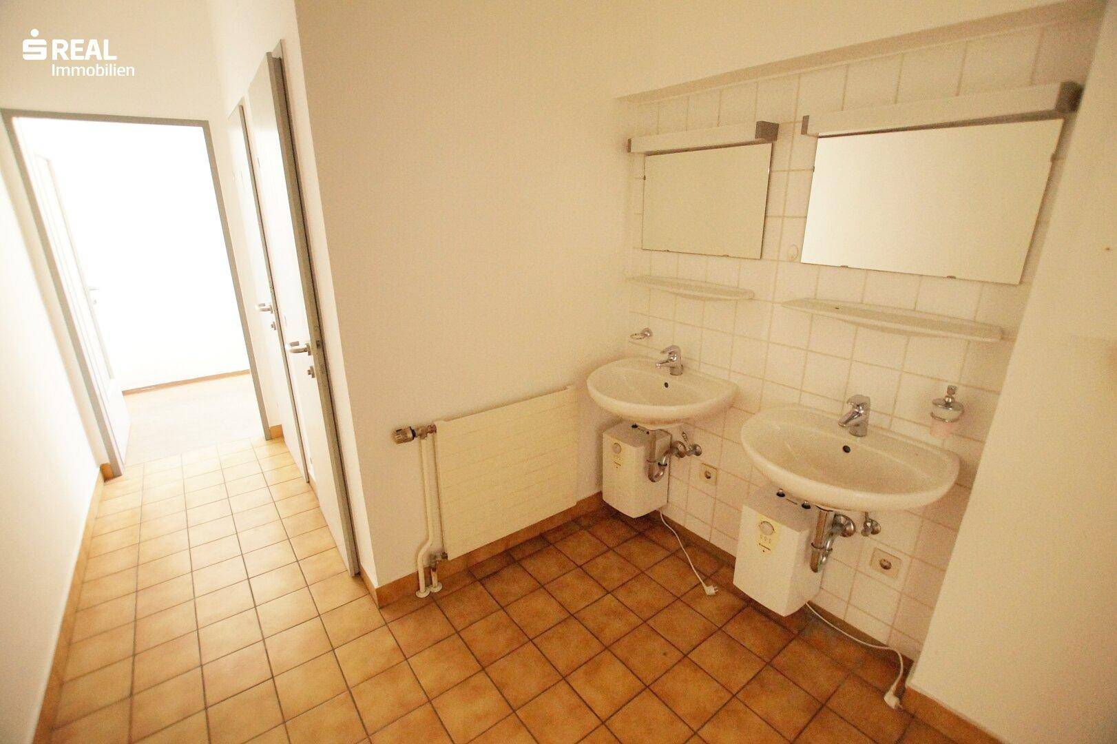 Badezimmer mit zwei Waschbecken, Spiegelschränken und hellbraunen Fliesen.