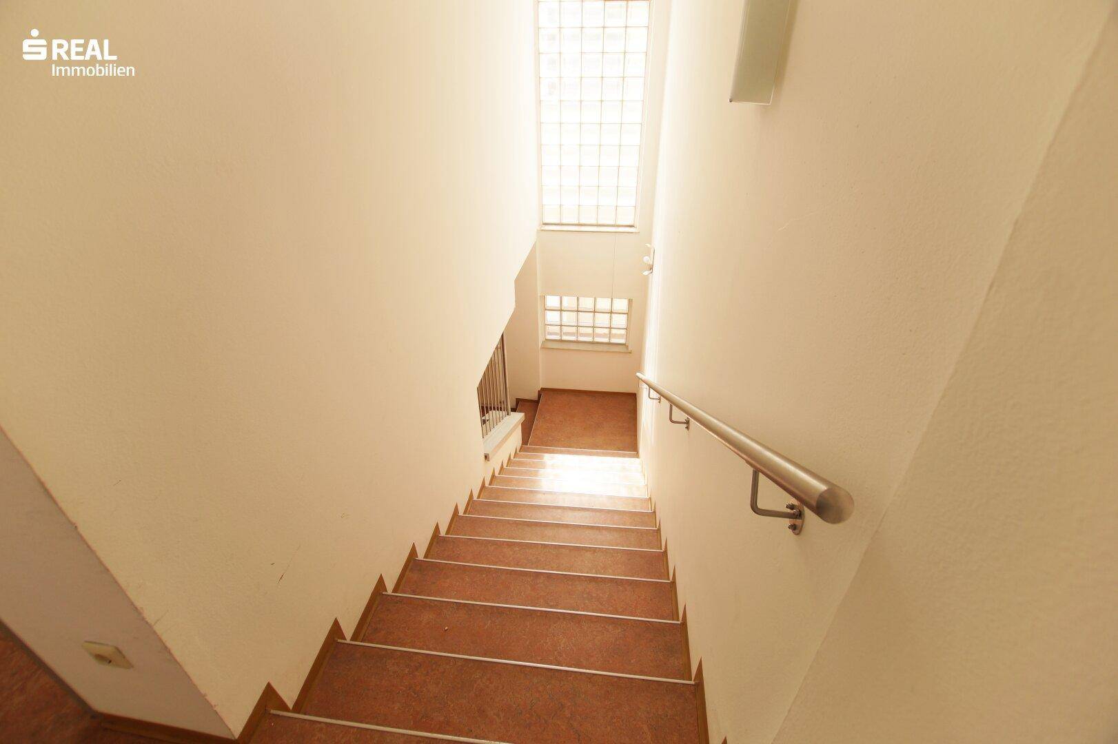 Treppenhaus mit Handlauf und Glasbaustein-Fenstern, die natürliches Licht hereinlassen.