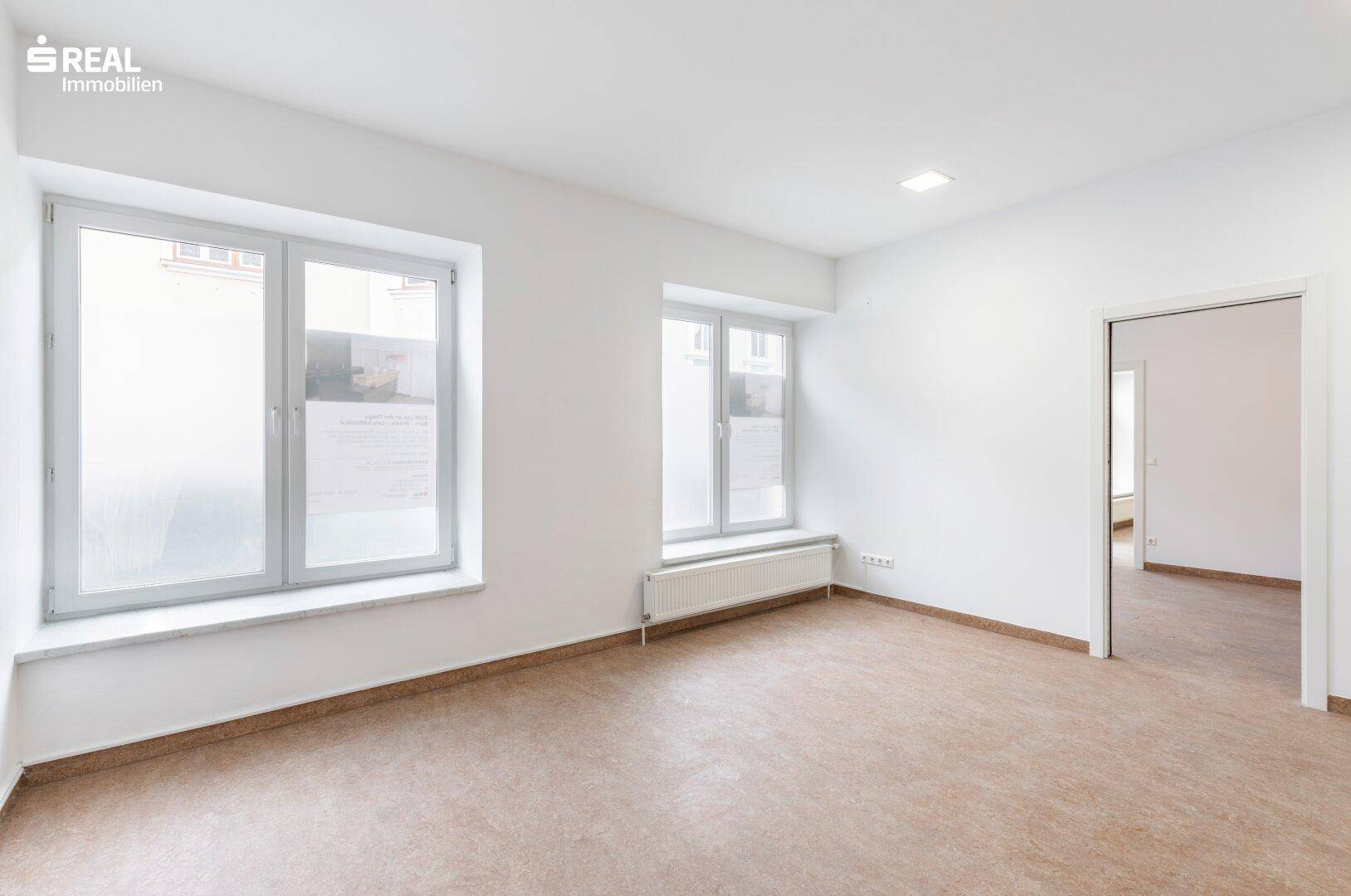 Geräumiger Raum mit zwei Fenstern unterschiedlicher Größe und einem Heizkörper, ideal für flexible Nutzung.
