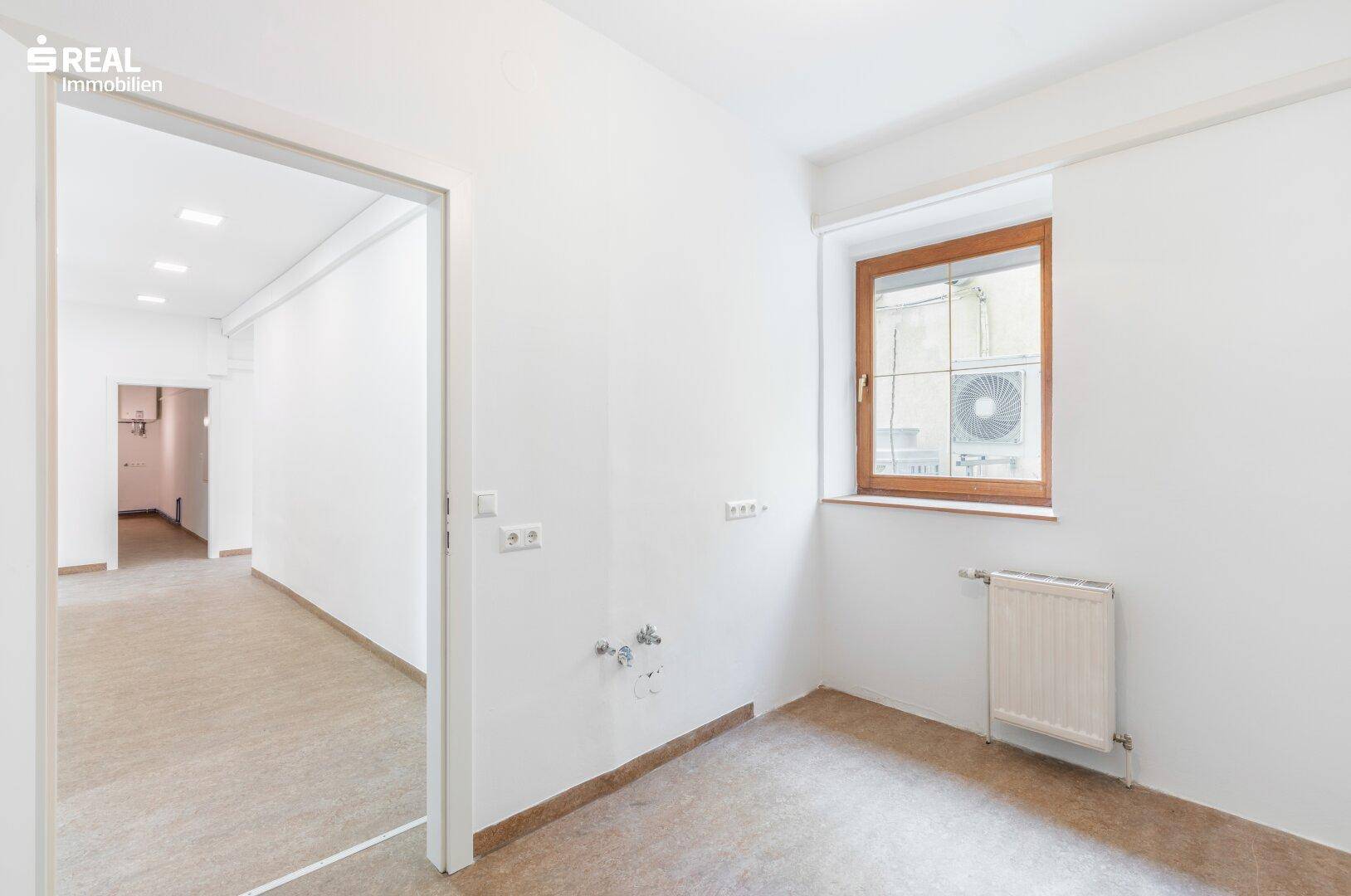 Raum mit Holzfensterrahmen, Heizkörper und sichtbaren Installationen, Blick auf eine Klimaanlage.