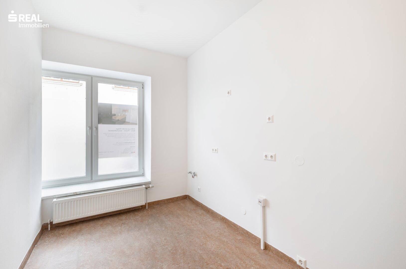 Raum mit großem Fenster, Heizkörper und sichtbaren Wandinstallationen, bereit für individuelle Gestaltung.