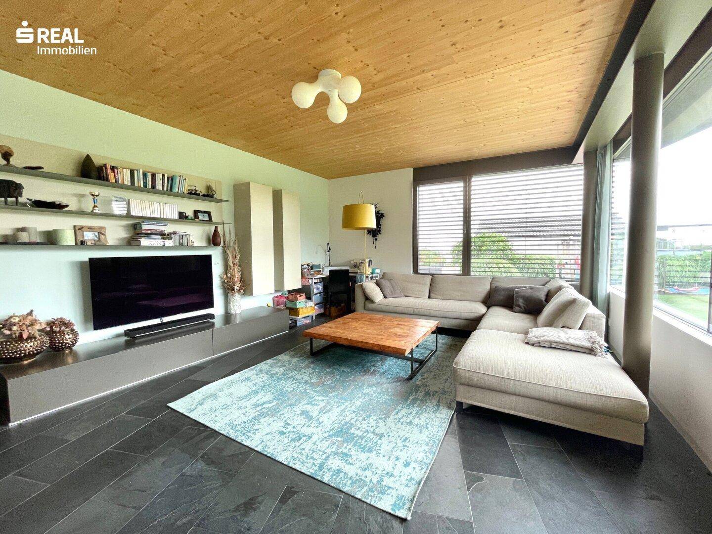 Helles Wohnzimmer mit Holzbalkendecke, großen Fenstern und modernem Interieur.