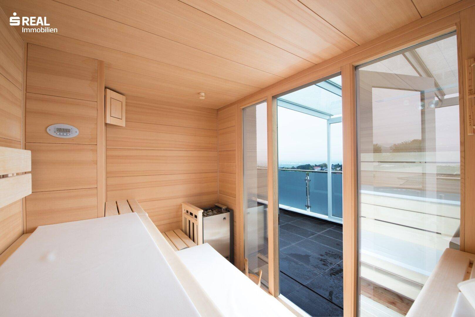 Moderne Holzsauna mit Glasfront und direktem Zugang zu einer Außenterrasse mit Weitblick.