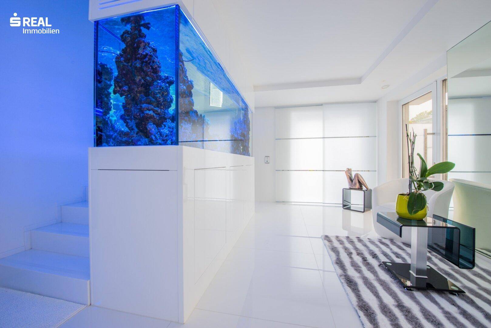 Moderner Eingangsbereich mit großem, beleuchtetem Aquarium und glänzenden weißen Fliesenboden.