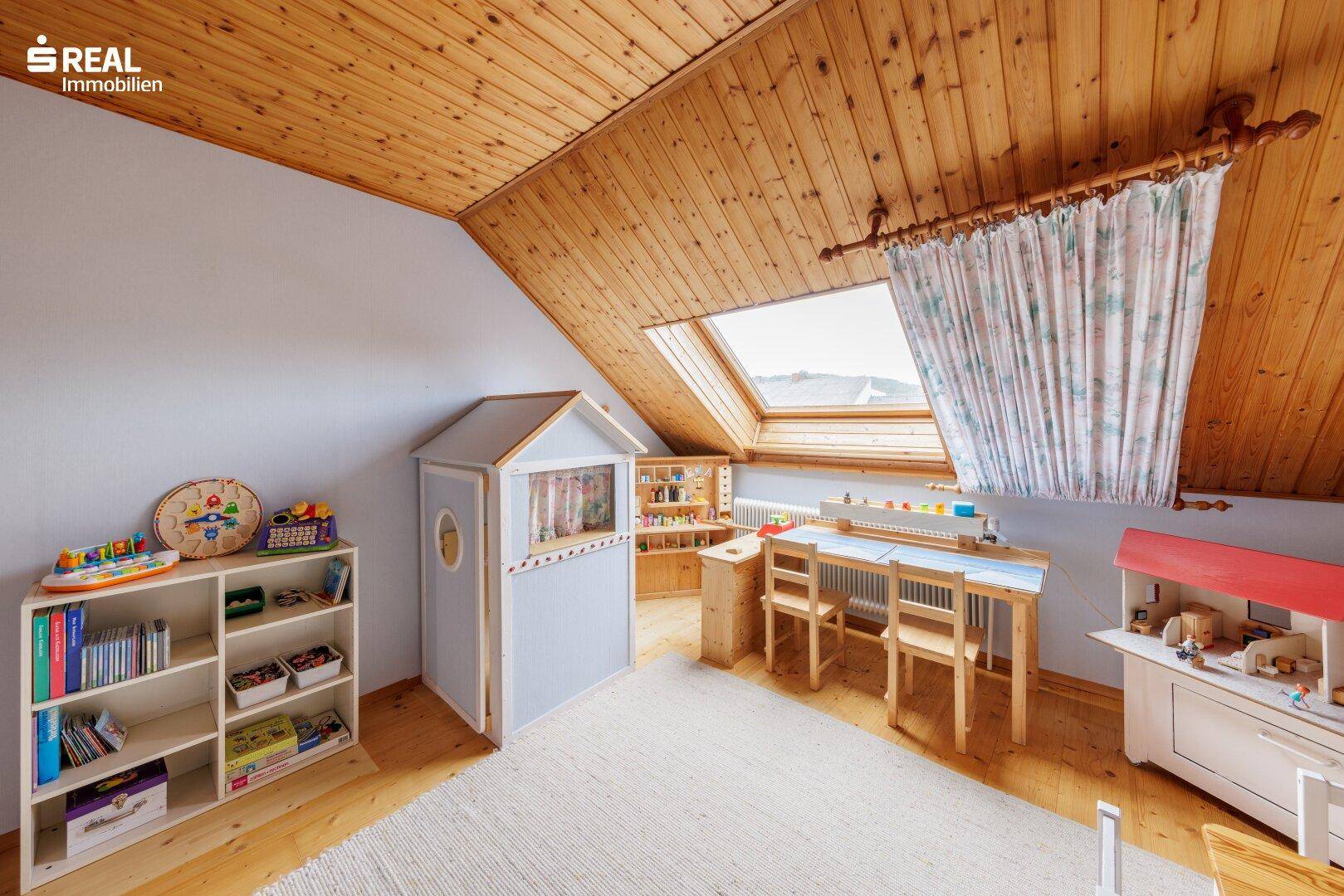 Kinderzimmer im Dachgeschoss mit Holzboden, Spielbereich und einem Dachfenster für viel Licht.