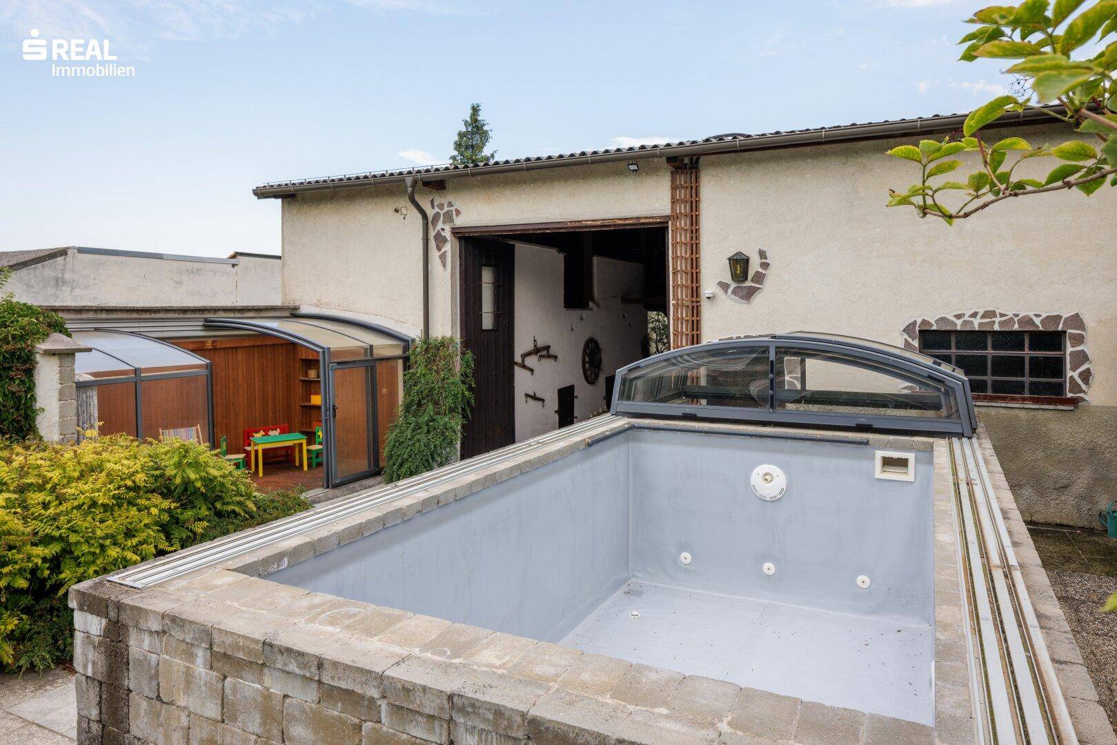 Außenbereich mit einem eingelassenen Pool oder Whirlpool und einem kleinen Gewächshaus im Hintergrund.