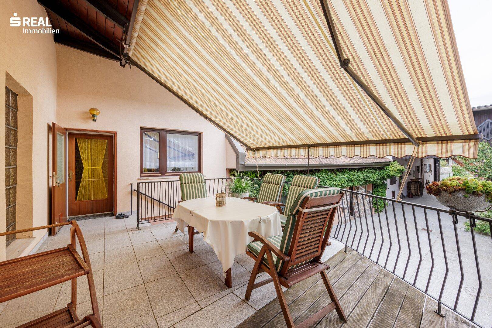 Geräumige Terrasse mit Markise, Gartenmöbeln und Blick auf den begrünten Außenbereich.
