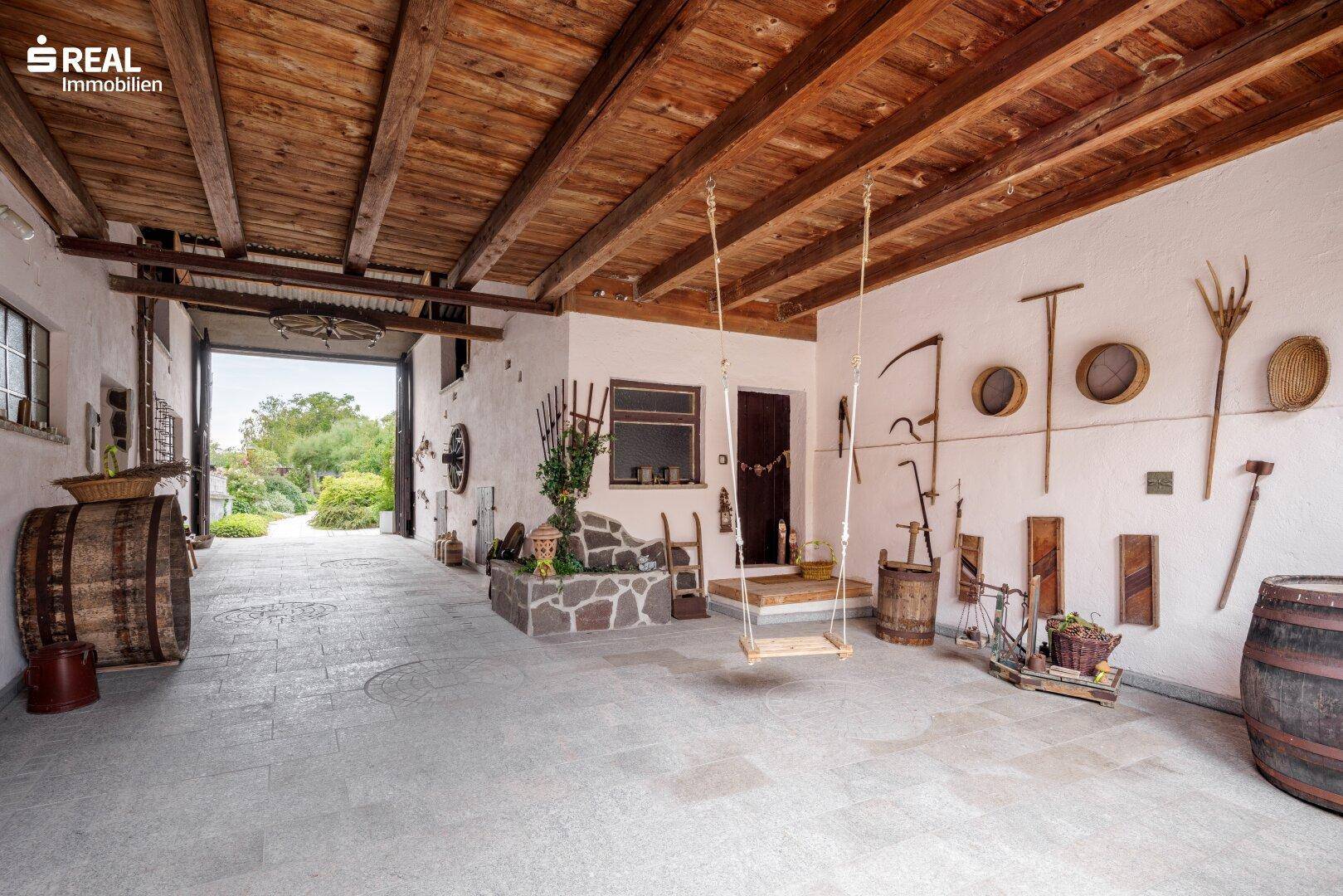 Großer überdachter Bereich mit Holzbalkendecke, Schaukel und traditionellen Werkzeugen an der Wand.