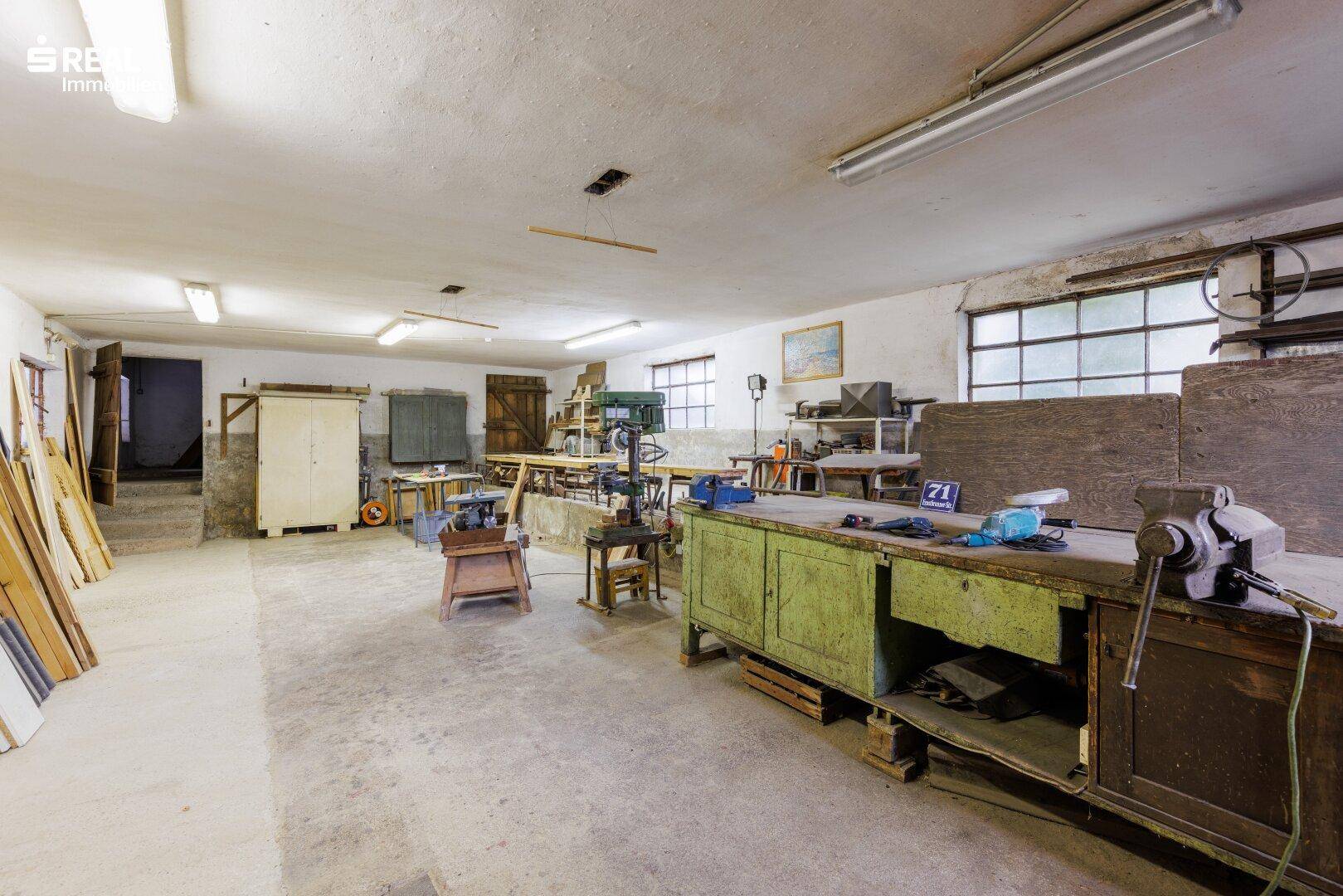 Geräumiger Werkstattraum mit Betonboden, Arbeitsflächen und Tageslicht durch mehrere Fenster.