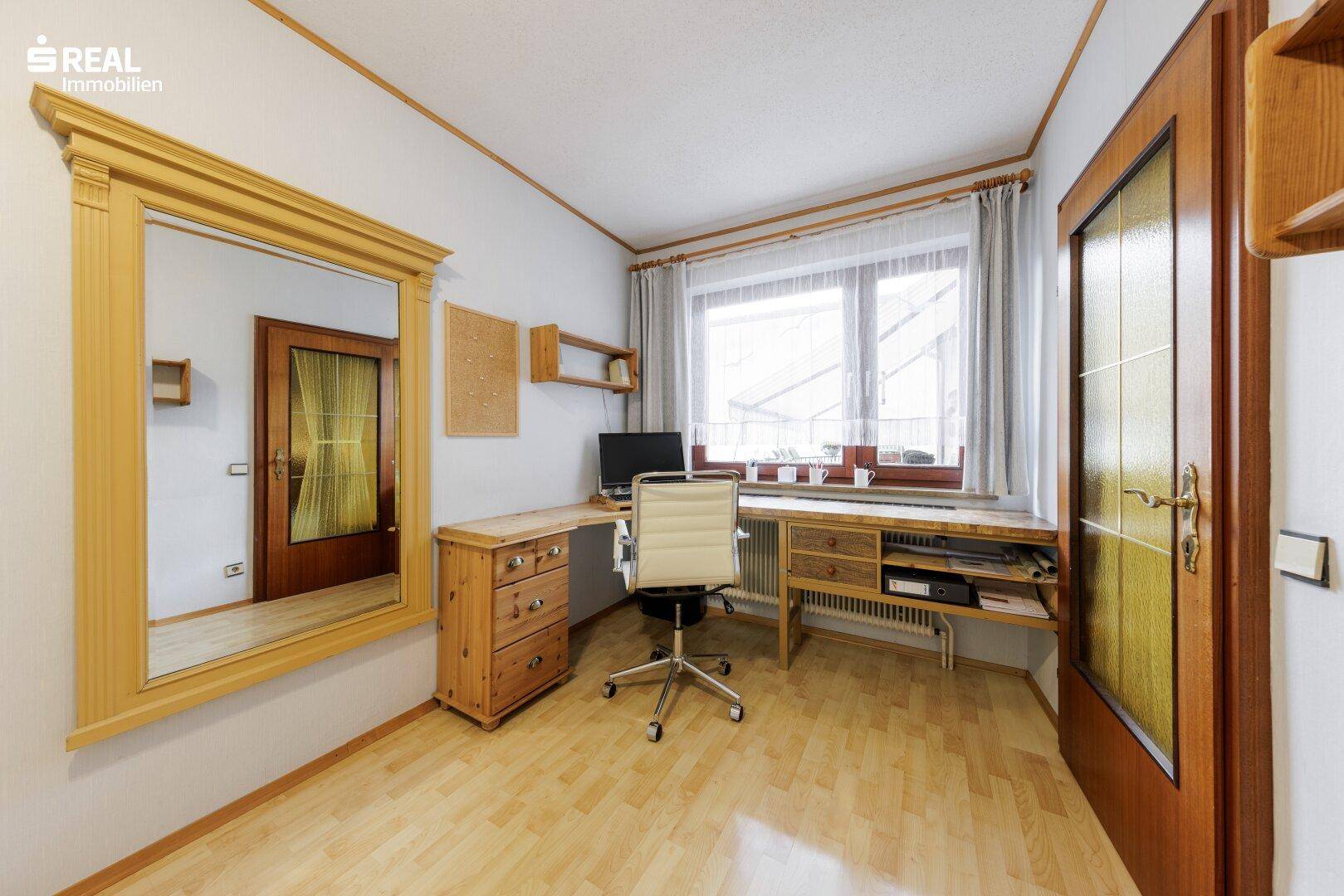 Funktionales Arbeitszimmer mit Holzschreibtisch, Bürostuhl und hellem Laminatboden.