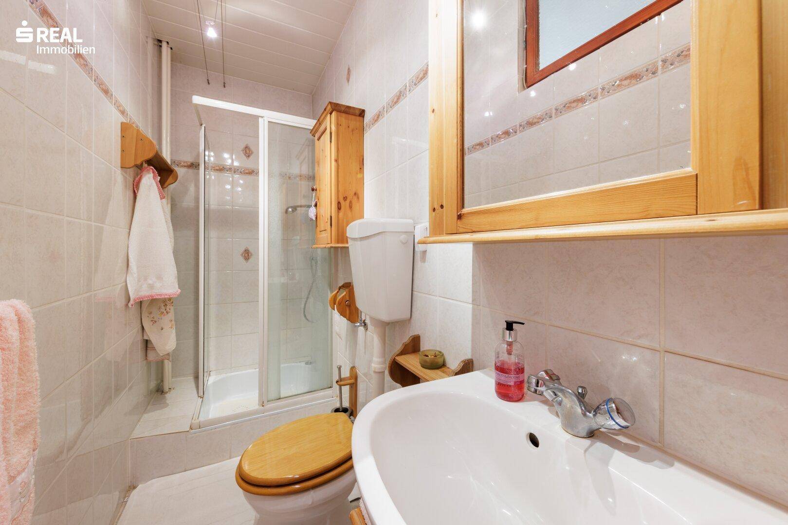 Kleines Badezimmer mit Dusche, WC, Waschbecken und hellen Fliesen.