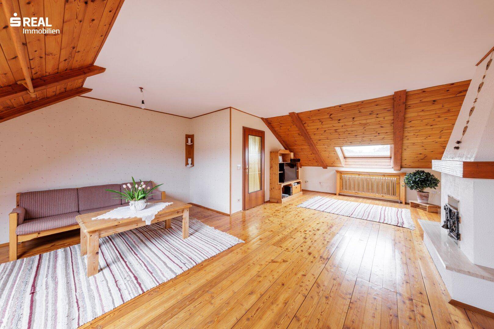 Gemütliches Wohnzimmer im Dachgeschoss mit Holzdielenboden, Dachschrägen und einem Kamin.
