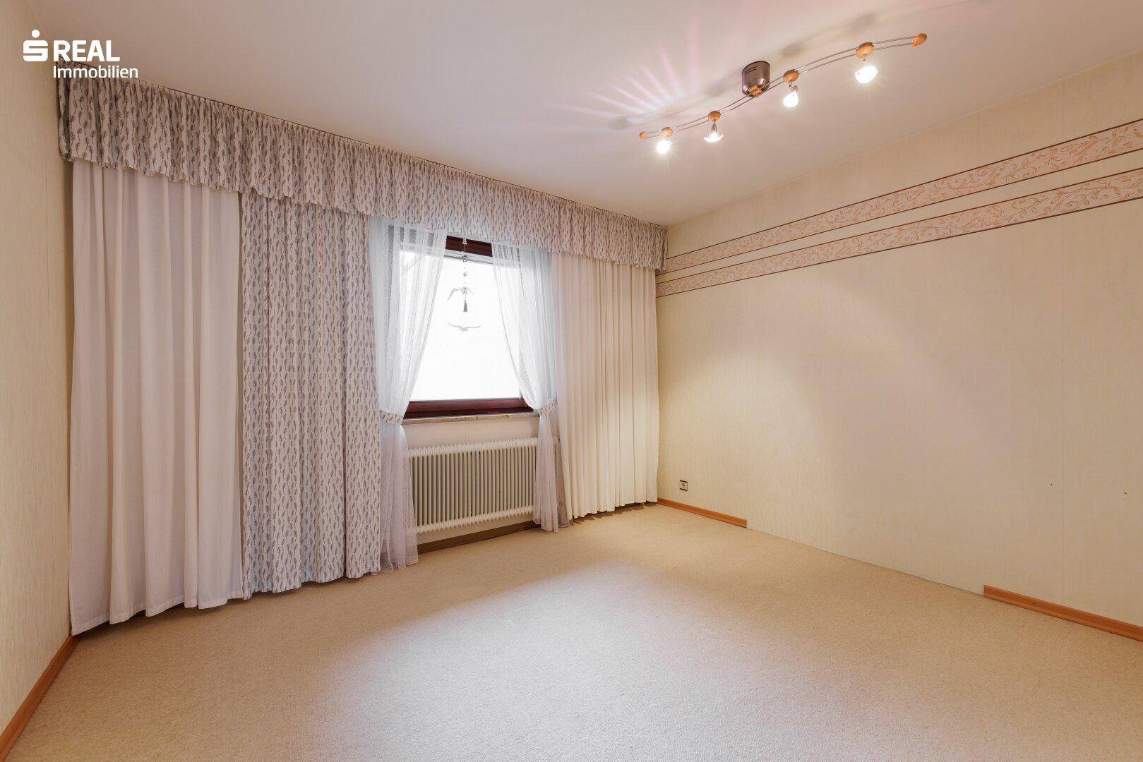 Leerer Raum mit Teppichboden, einem Fenster und einer schlichten Wandgestaltung.