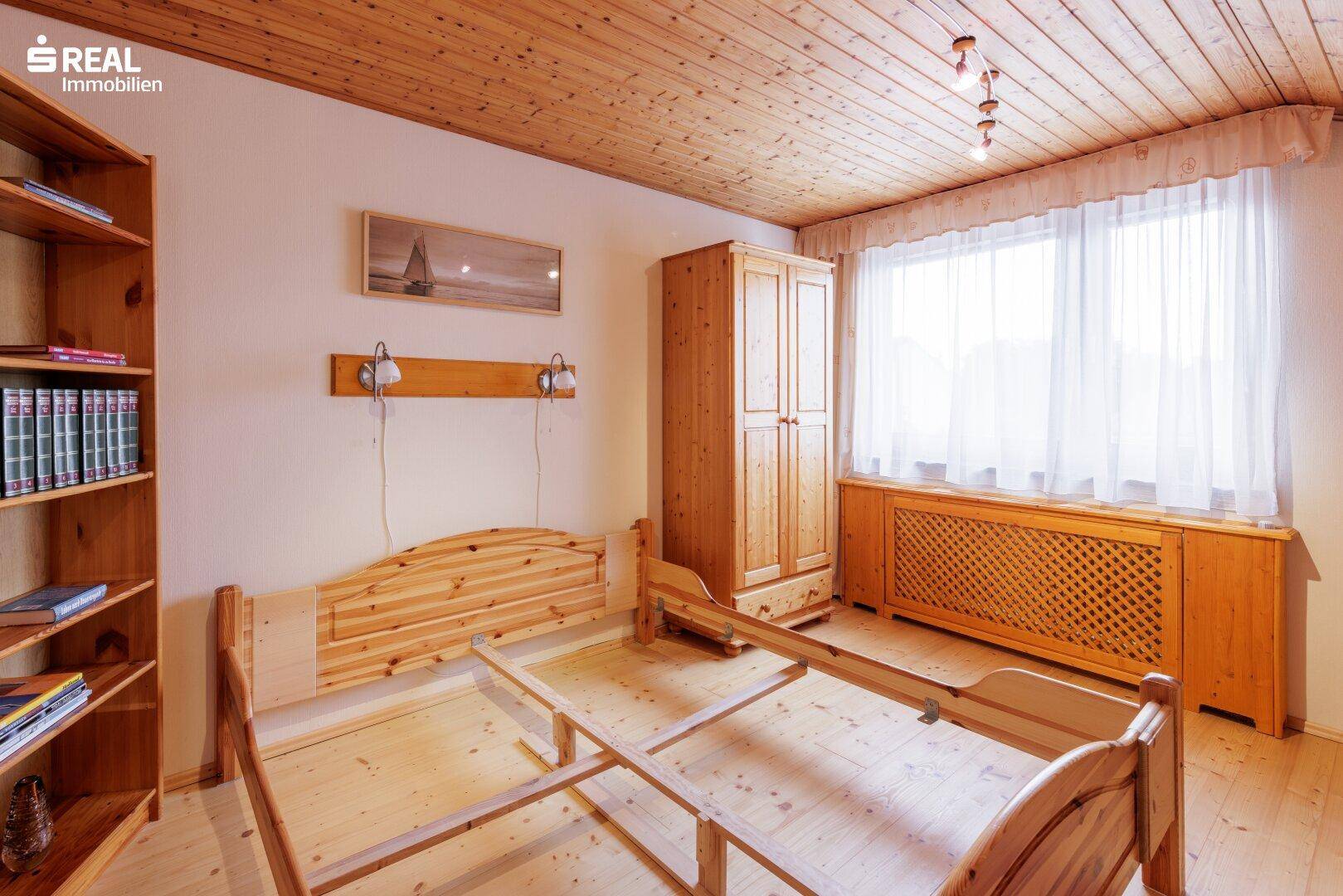 Helles Schlafzimmer mit Holzbett, Kleiderschrank und Holzbalkendecke, gut beleuchtet.